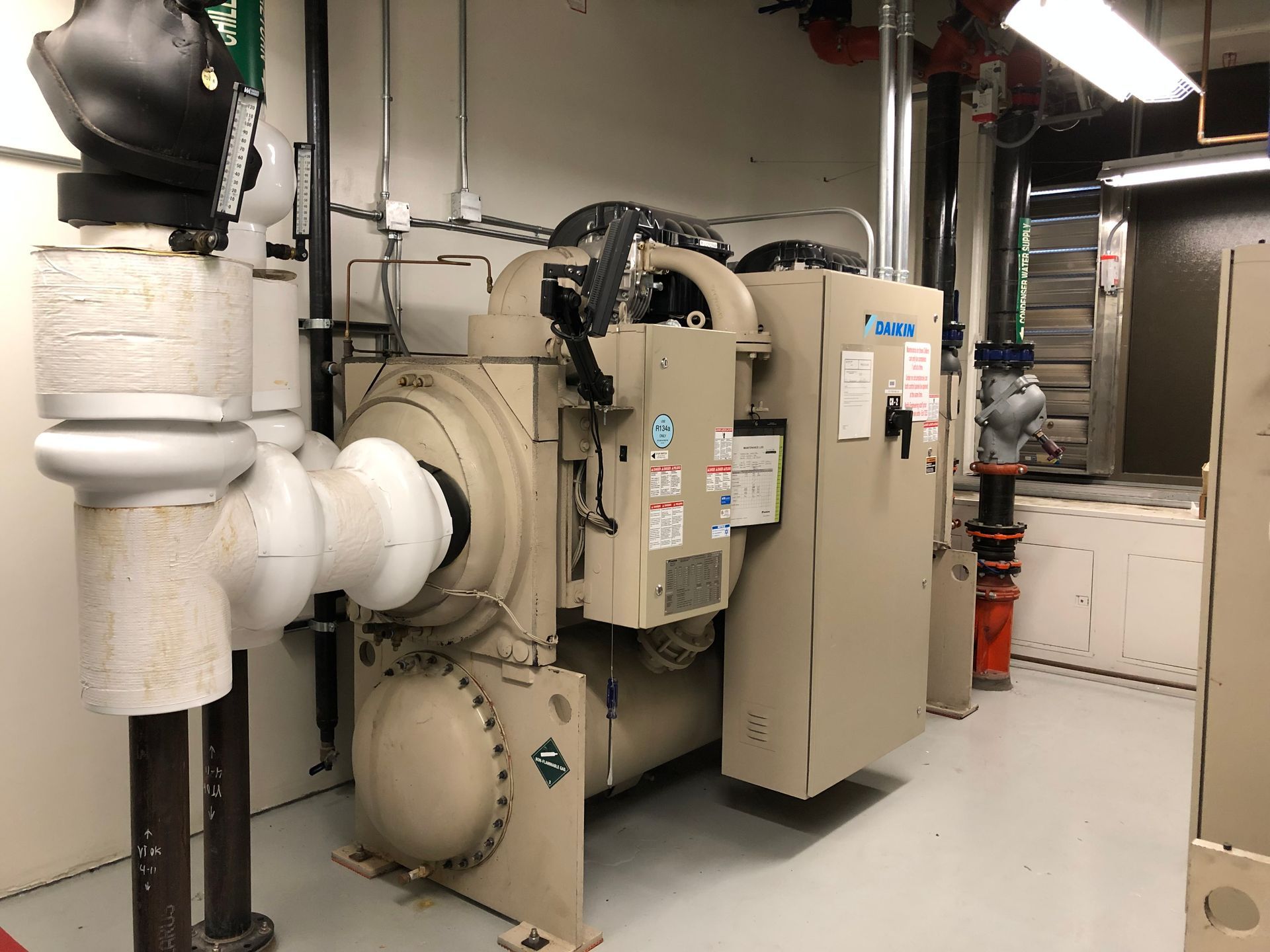 A large machine is sitting in a room next to pipes.