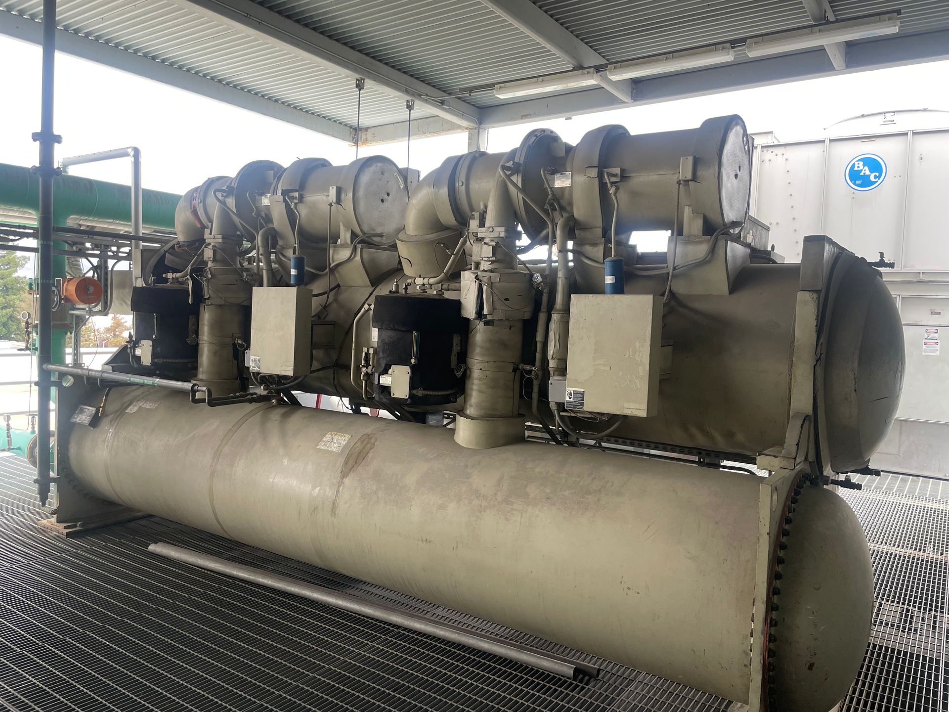A large chiller is sitting under a roof in a factory.