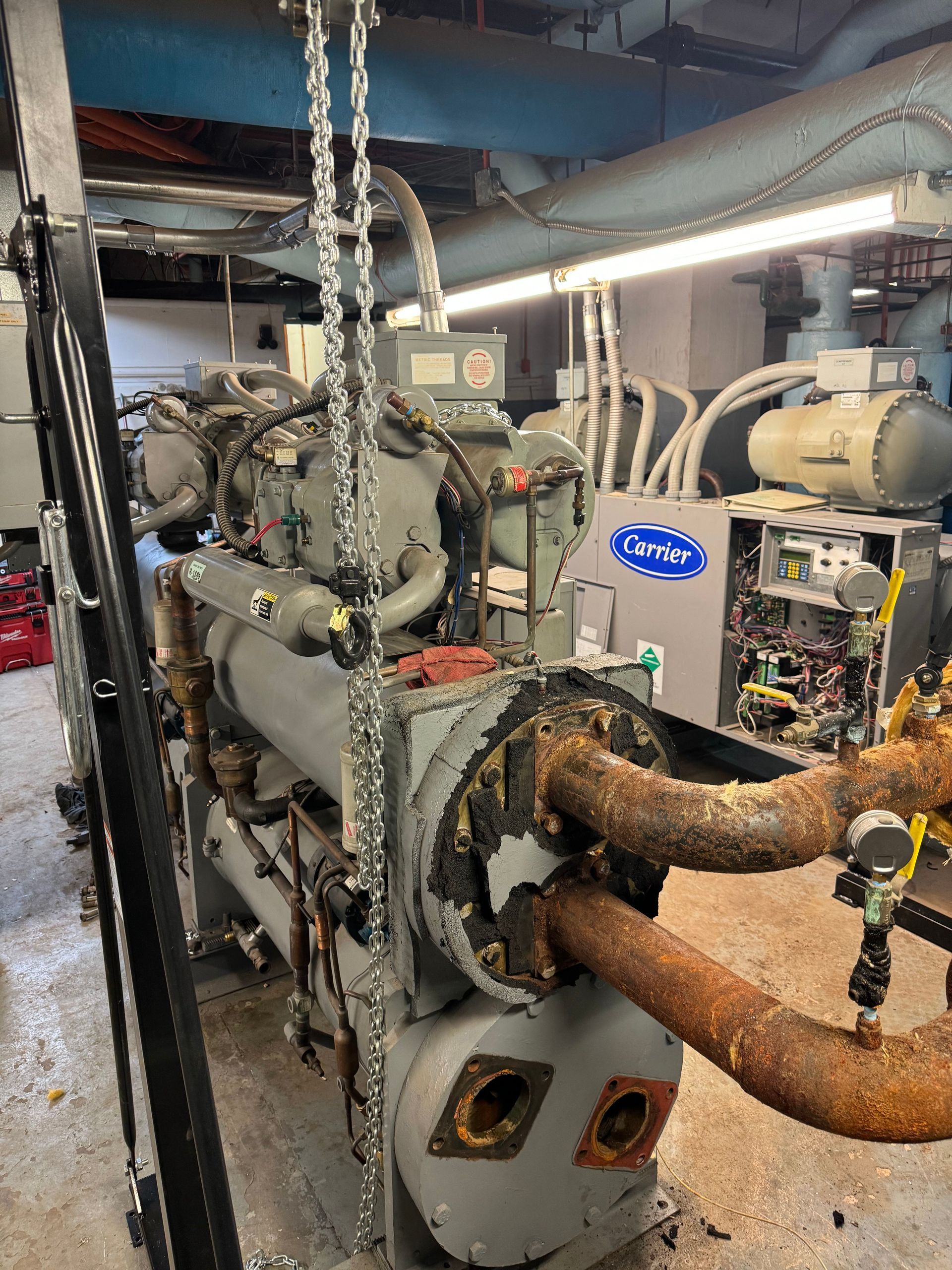 A large machine is sitting in a room with rusty pipes.