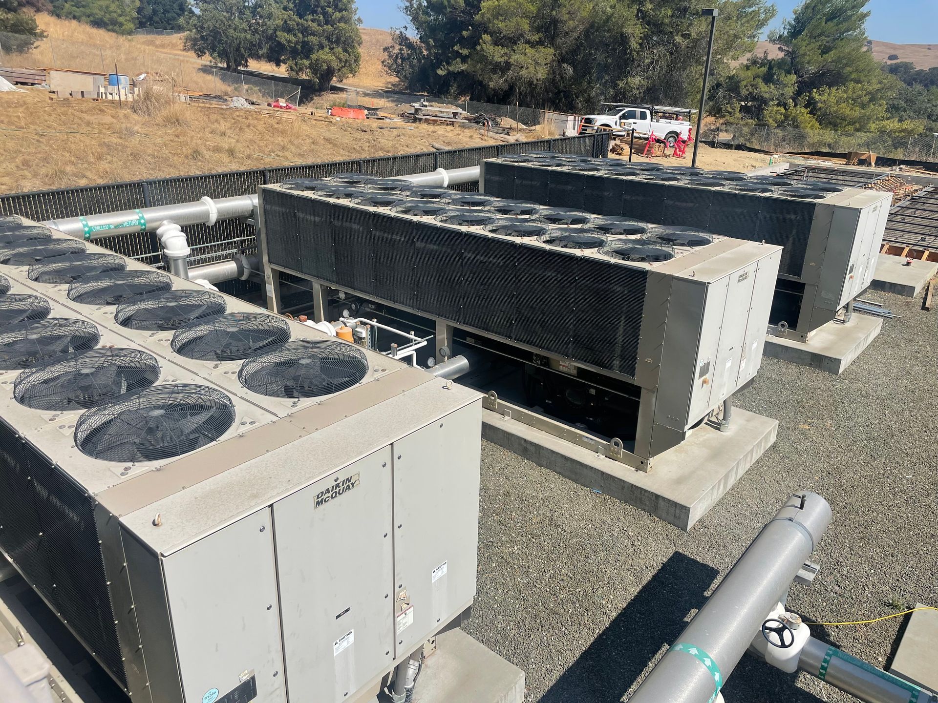 A row of air conditioners are sitting on top of a gravel area.