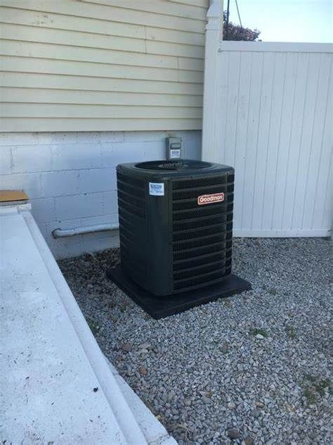 An air conditioner is sitting outside of a house next to a white fence.