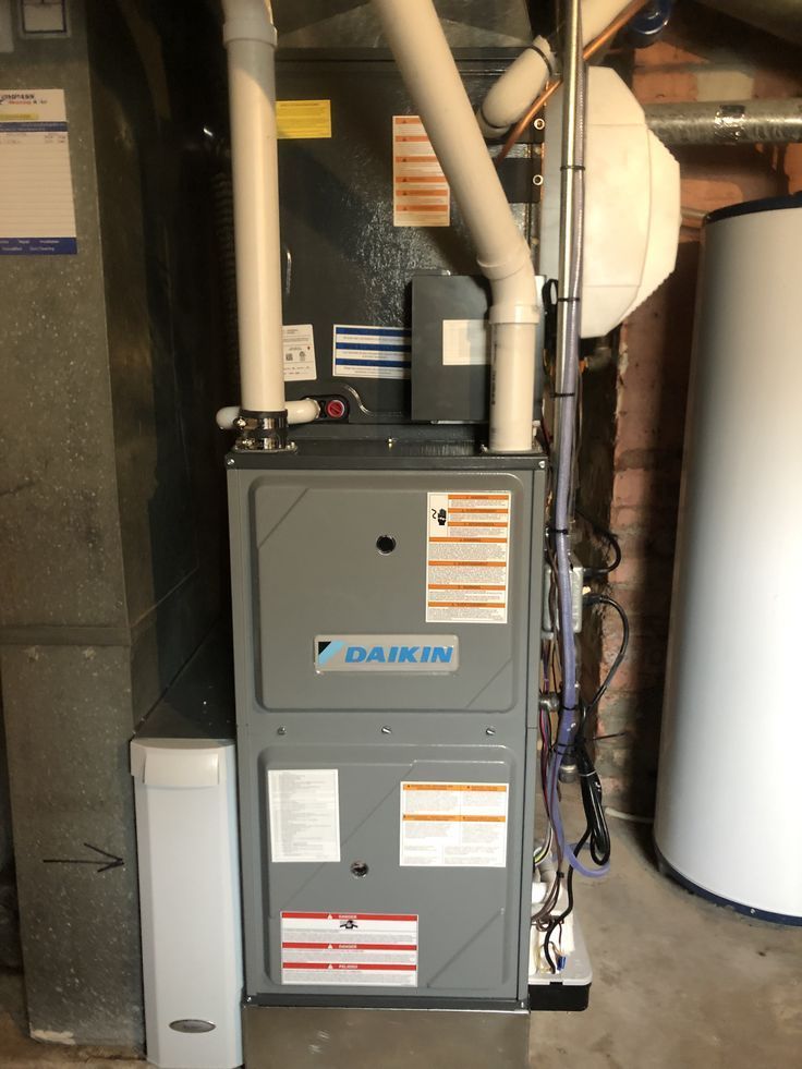 A daikin air conditioner is sitting in a basement next to a water heater.