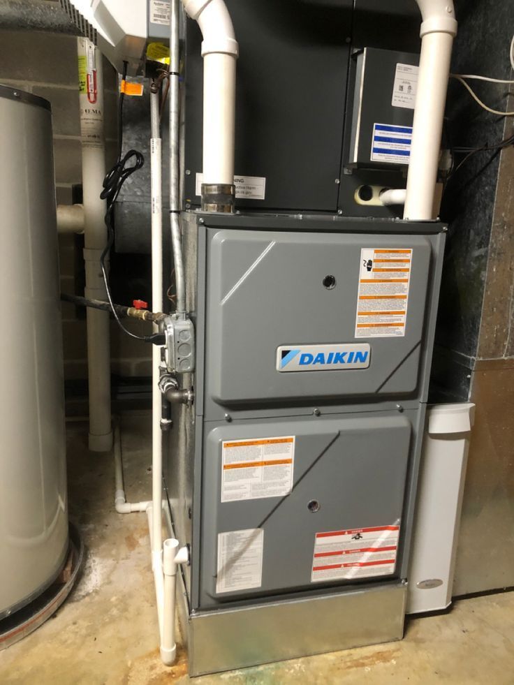 A daikin air conditioner is sitting in a basement next to a water heater.