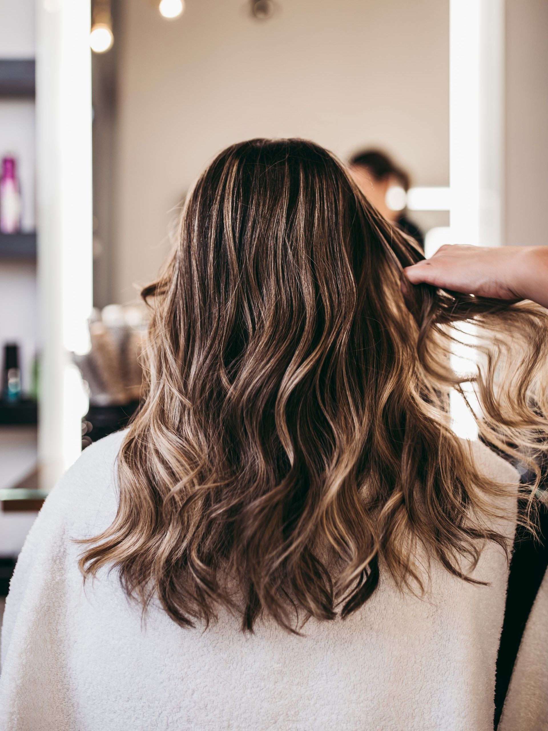 Woman getting her hair styled at a salon. Brown wavy hair with highlights being styled by a hand.