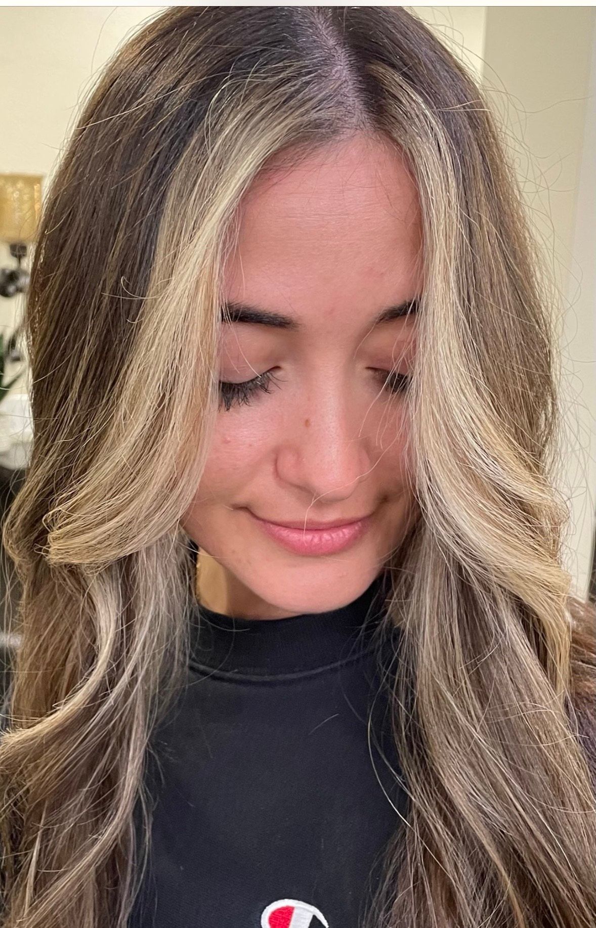 Woman with brown hair, face framed by blonde highlights, looking down and smiling.