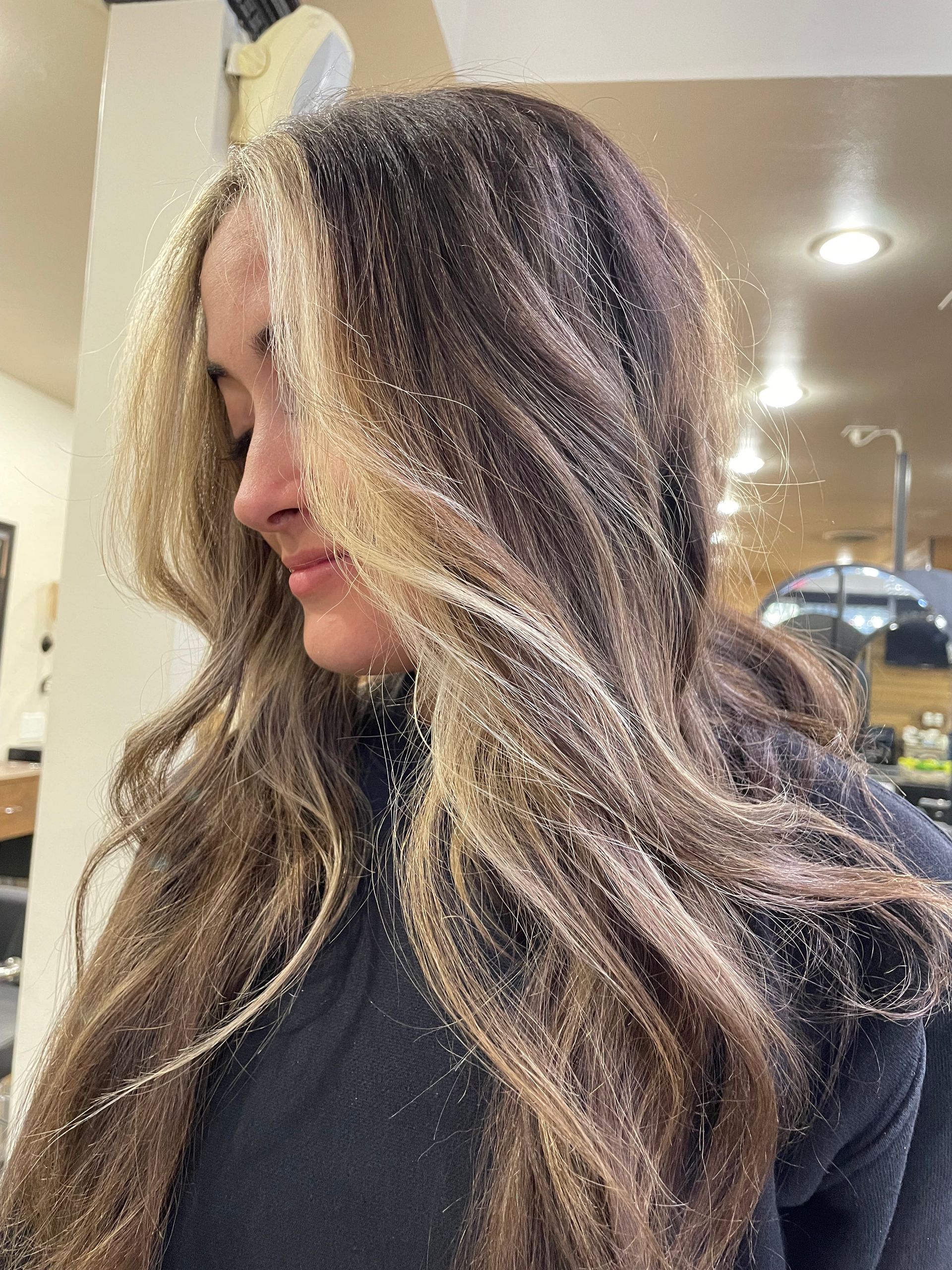 Woman with wavy brown hair highlighted with blonde. She is in a salon.