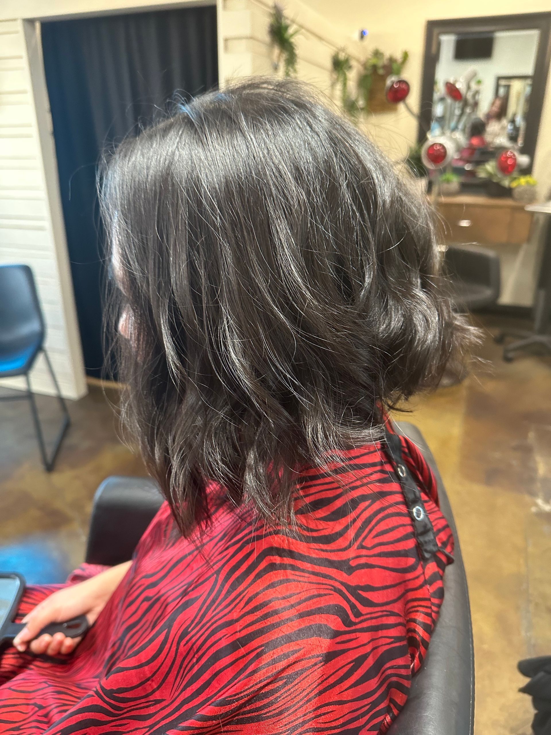 Woman with dark bob haircut, wearing a red and black patterned cape, in a salon.