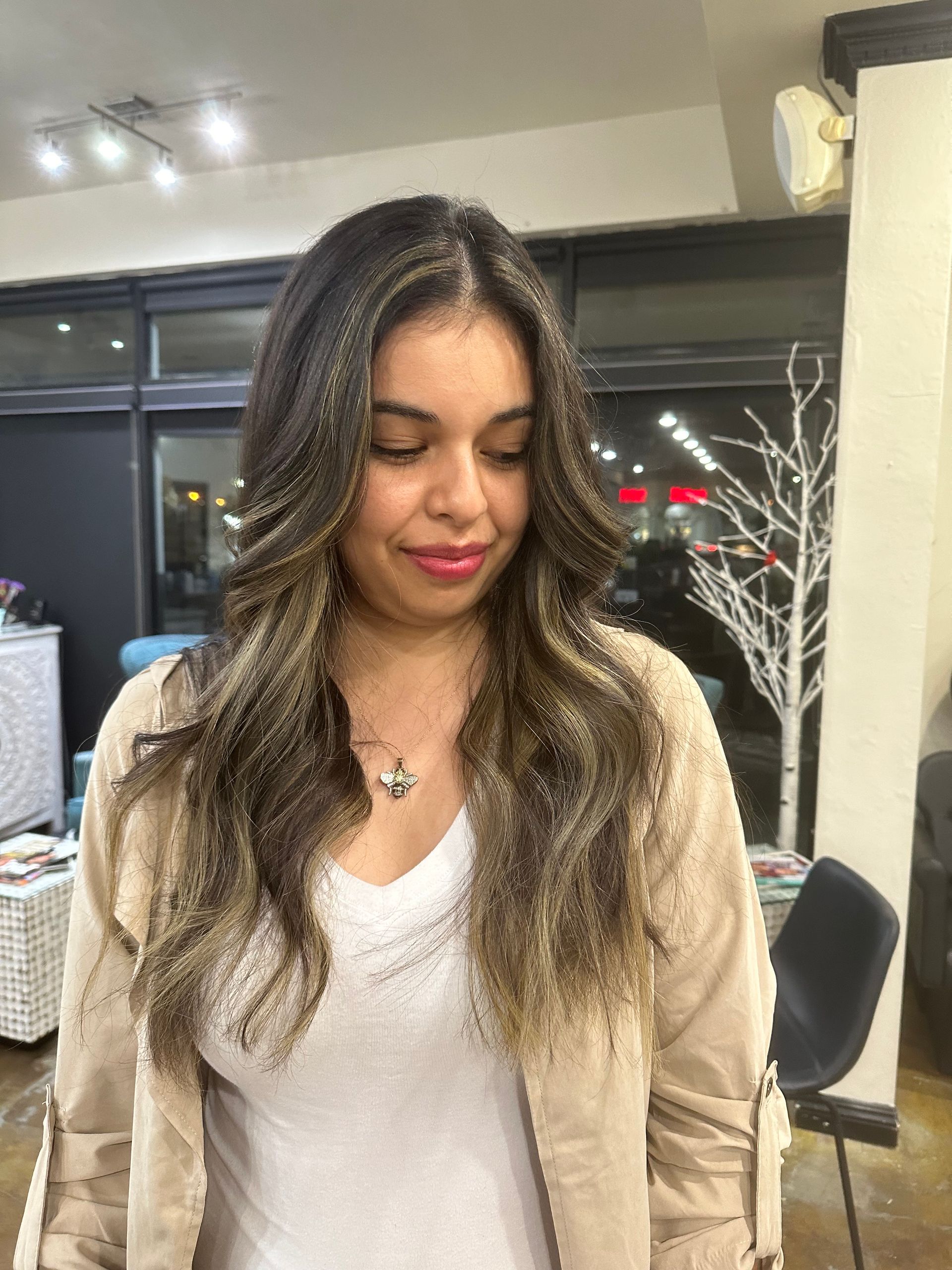 Woman with wavy brown hair, smiling, in a beige jacket and white shirt.