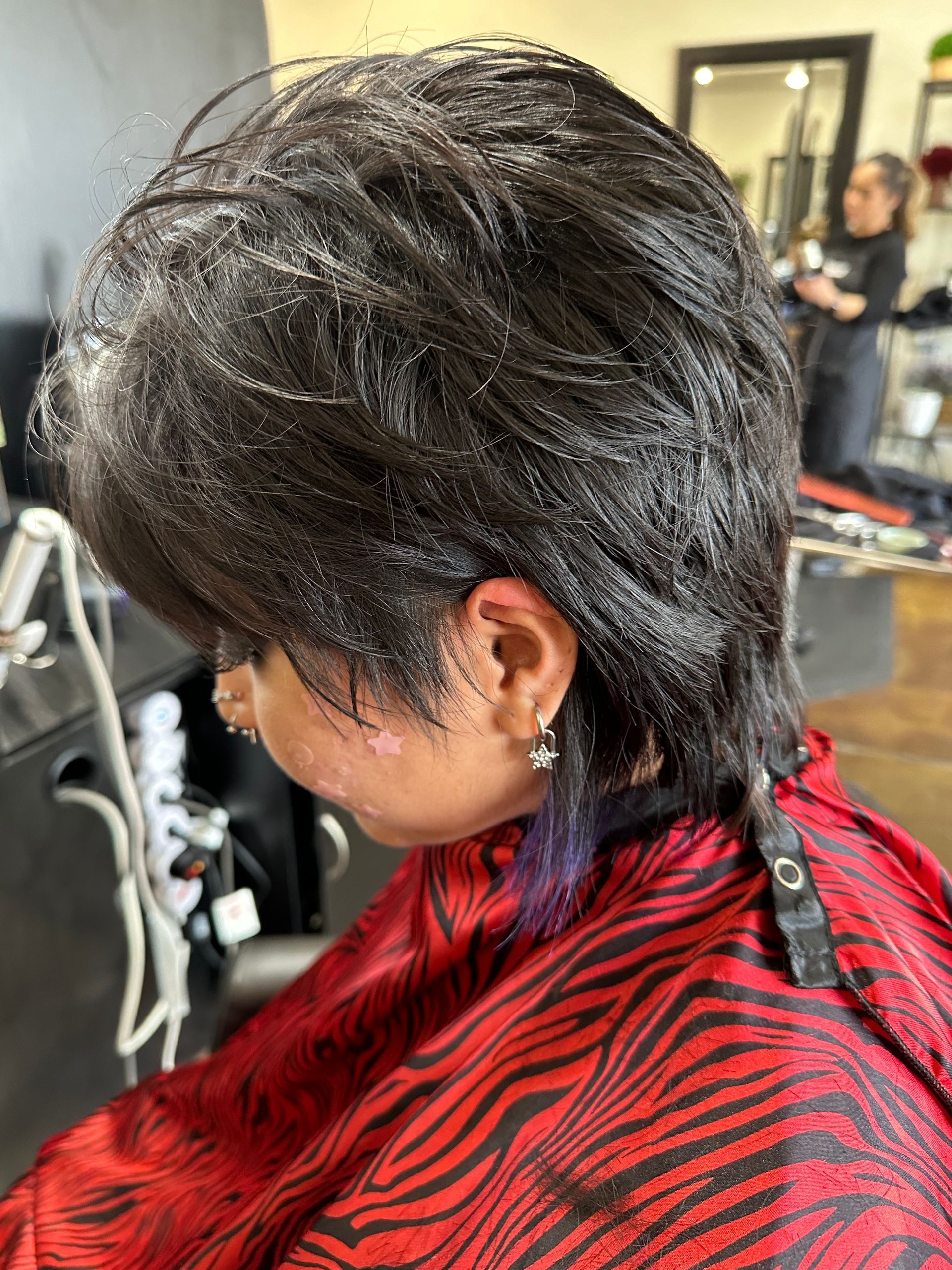 Woman with wet, layered black hair in a salon, wearing a red and black cape.