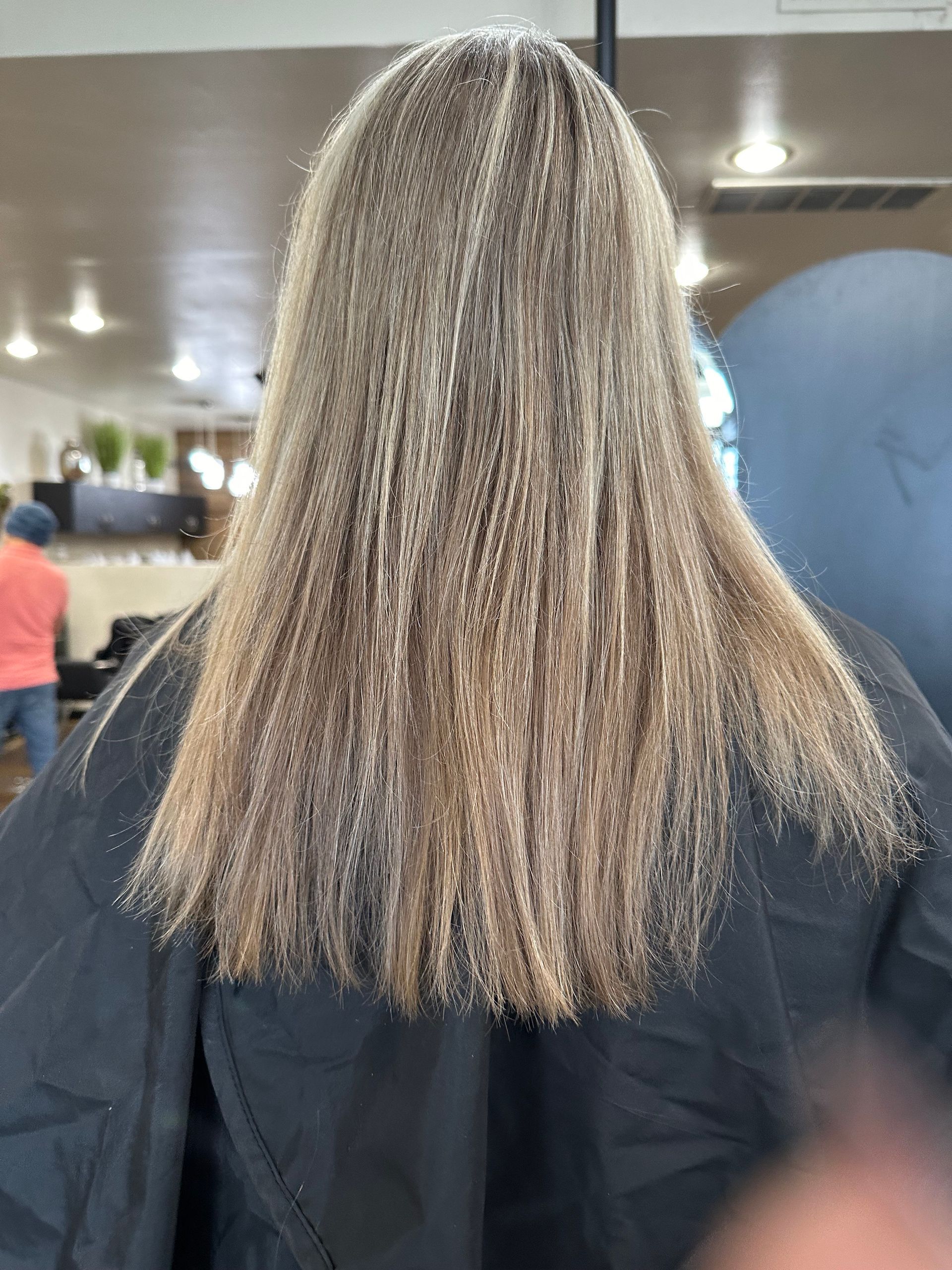 Woman with long crimped hair, viewed from the back, in a salon setting.