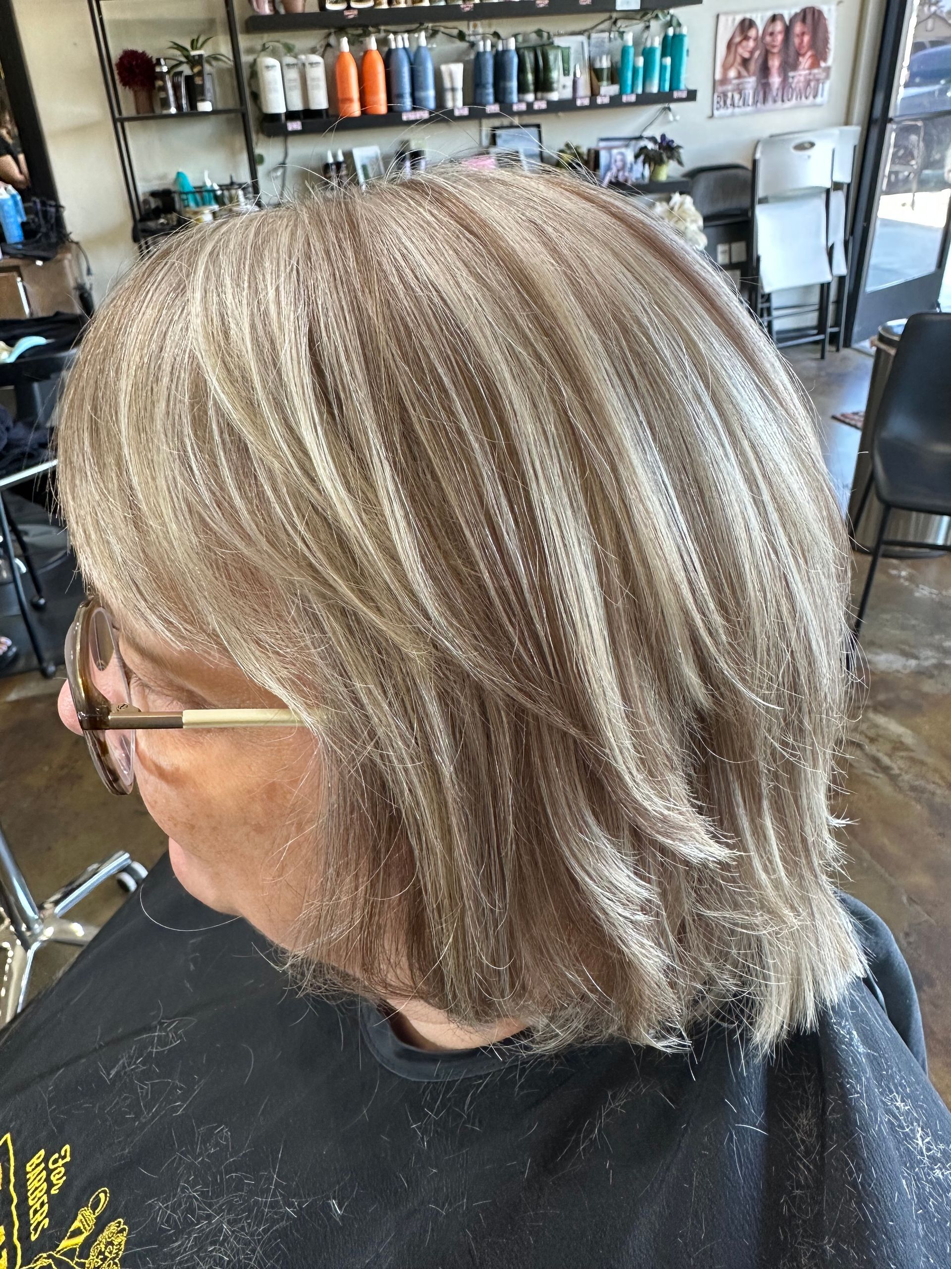 Woman with layered, ash-blonde hair at a salon, with a dark shirt covered in hair.