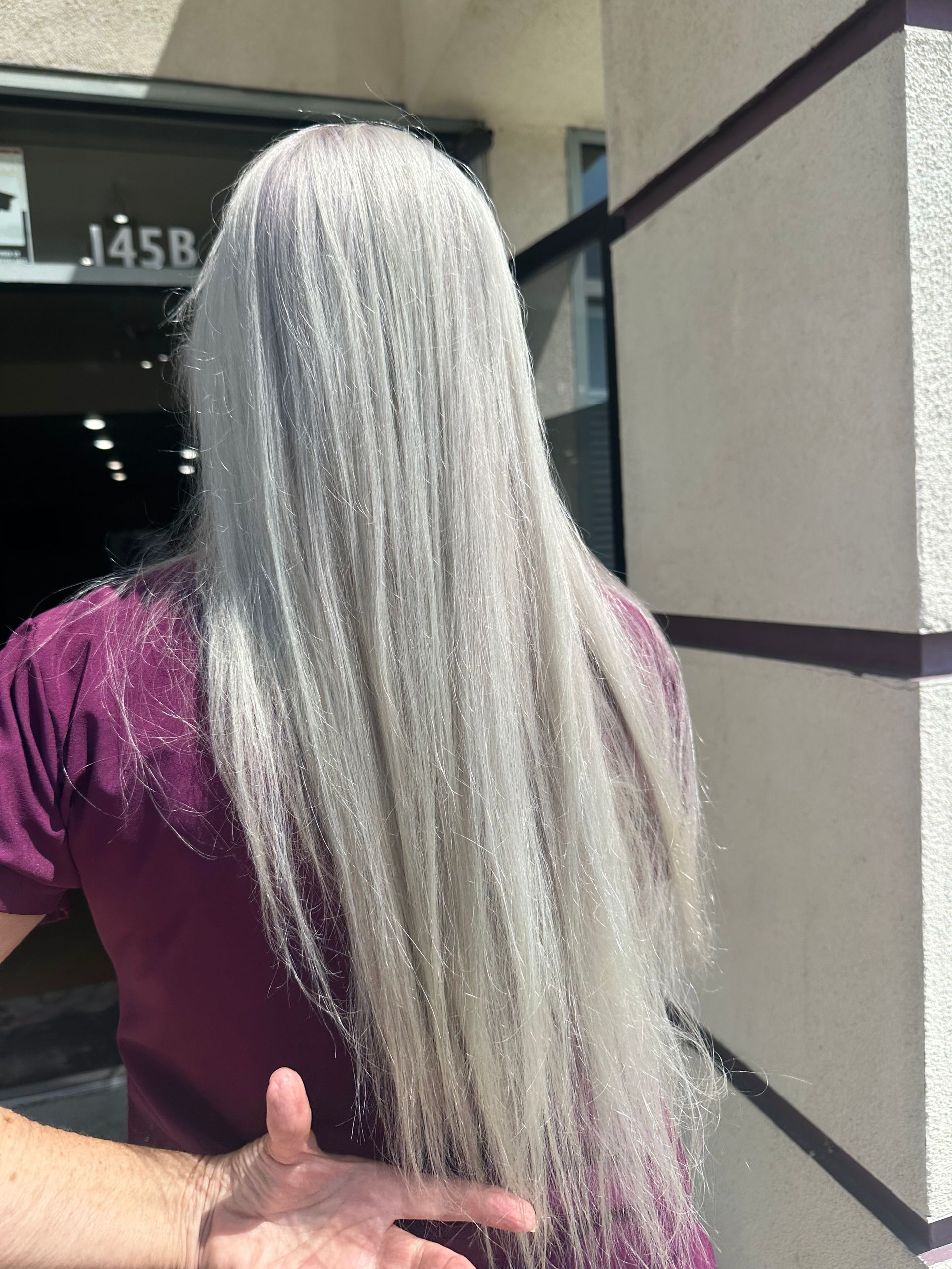 Person with long, silvery-gray hair wearing a maroon shirt, standing outside a building.