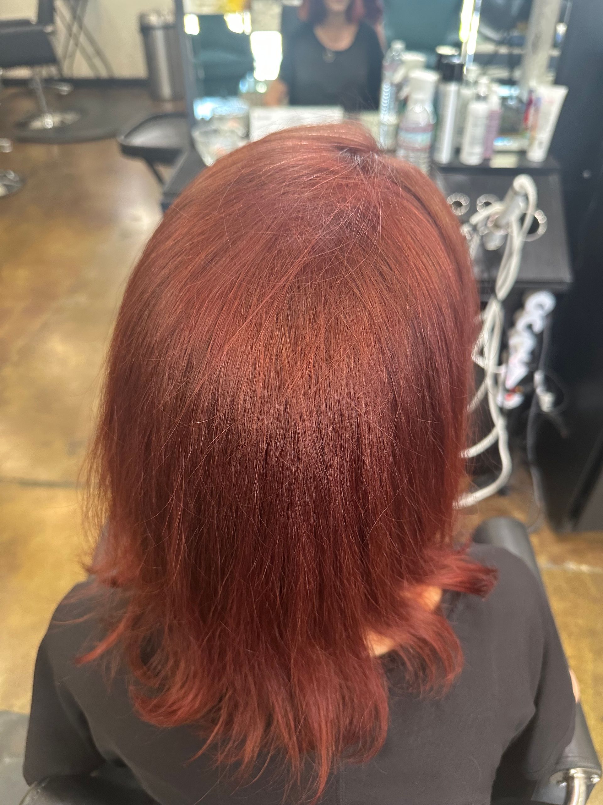 Woman with auburn hair sitting in a salon chair. Dark setting, tools in background.