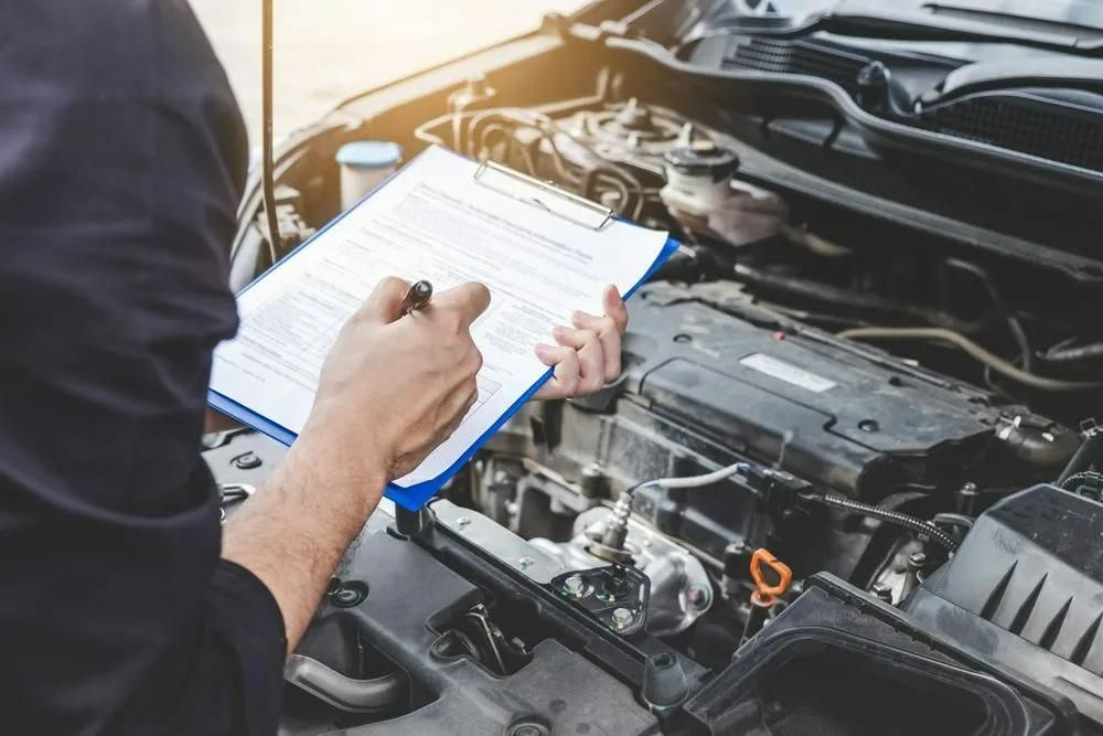 A Man Is Looking Under the Hood of A Car While Writing on A Clipboard — Coalfields Mechanical & Towing in Blackwater, QLD