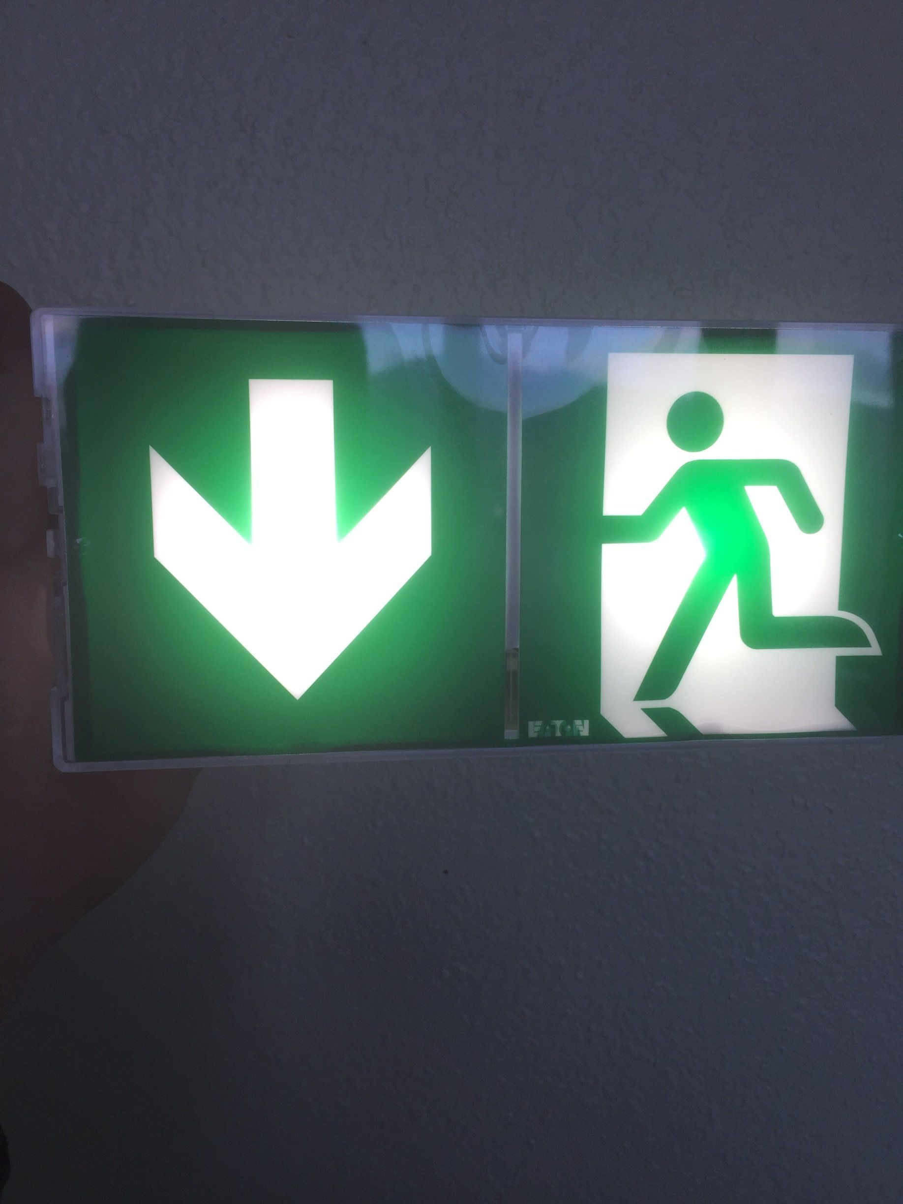 Un panneau de sortie vert avec une flèche pointant vers le bas et un homme qui court