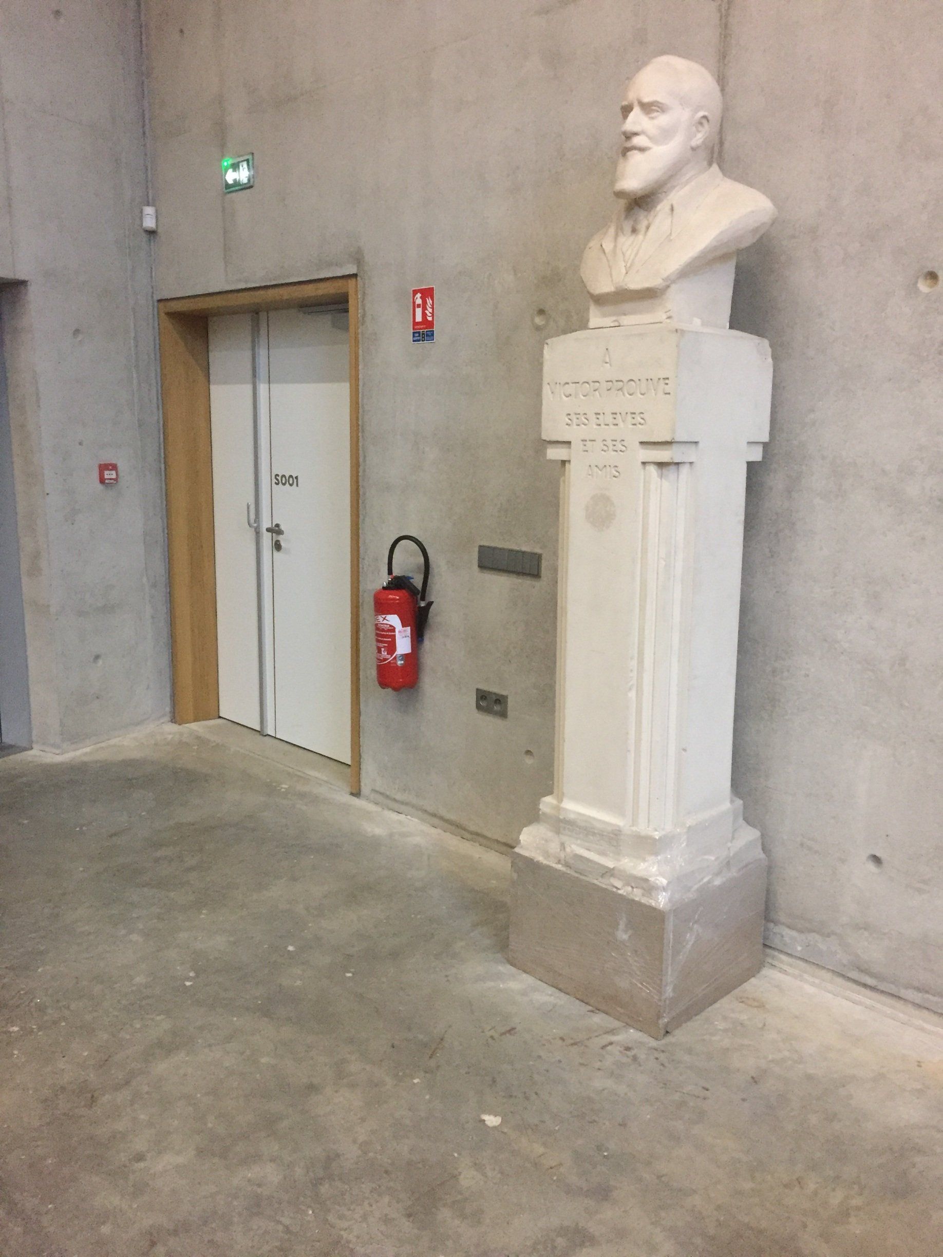 Une statue d'un homme avec une barbe se trouve dans un couloir à côté d'un extincteur