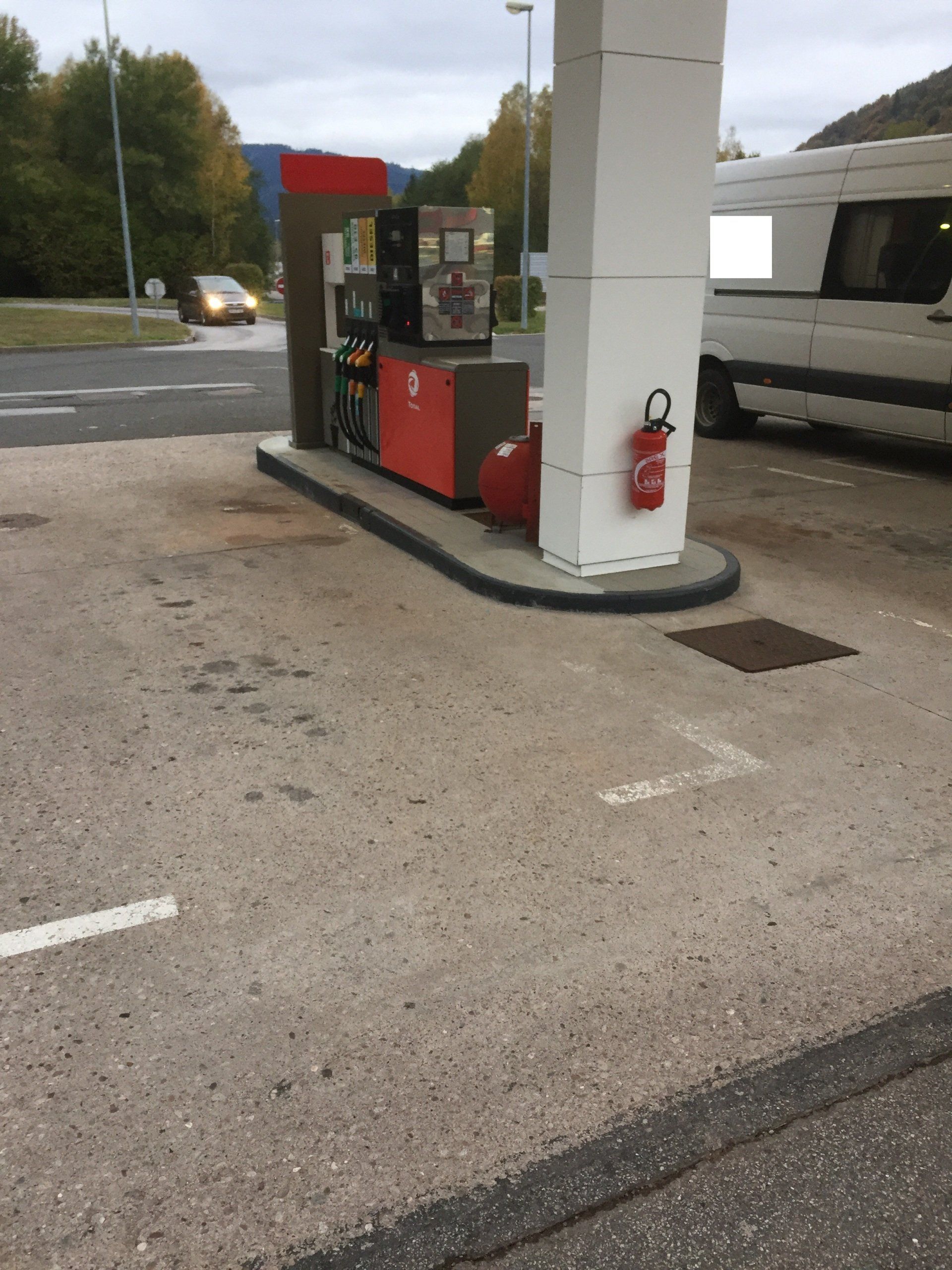 Une camionnette blanche est garée à côté d'une pompe à essence