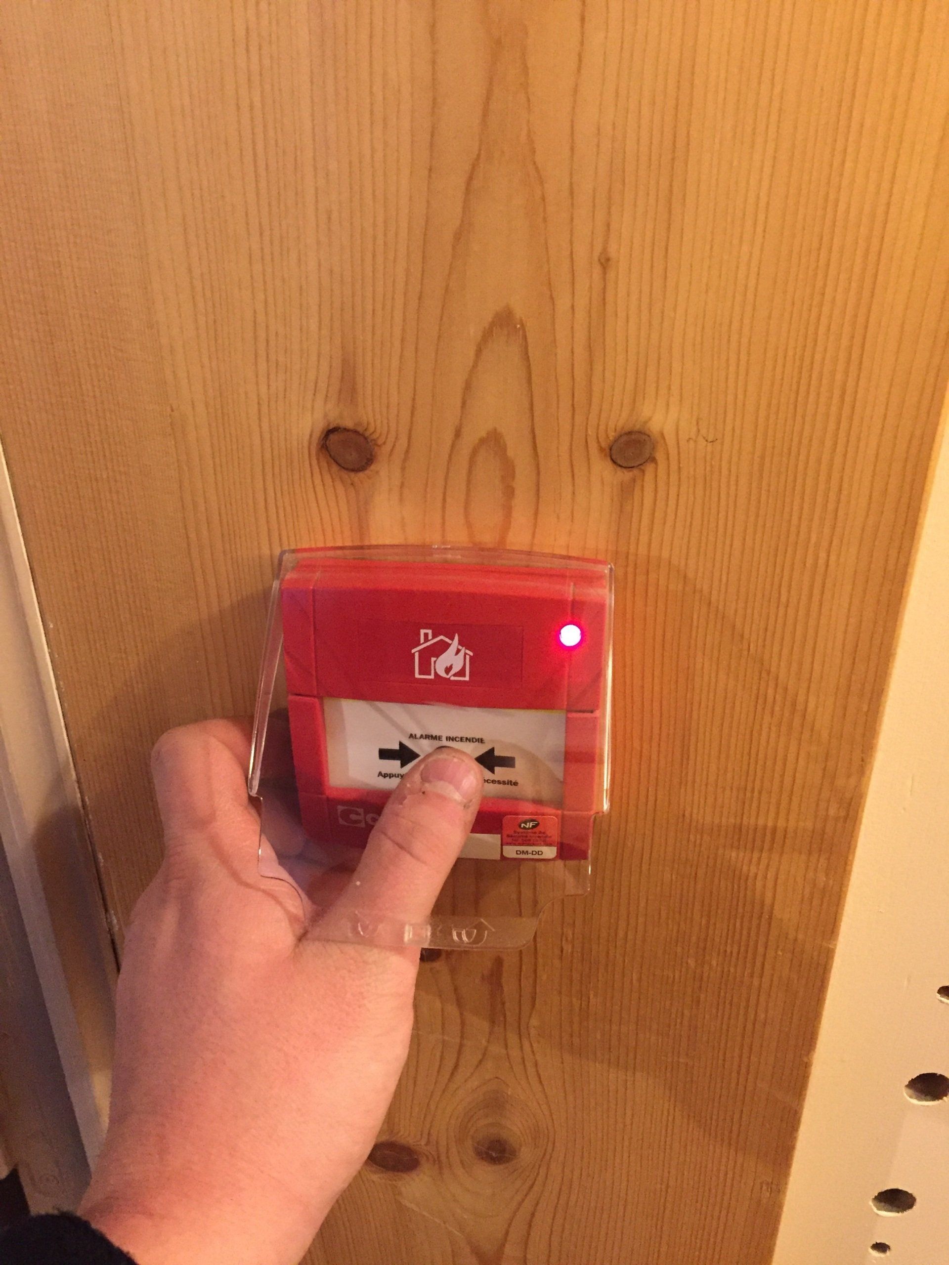 Une personne appuie sur un bouton rouge sur une porte en bois.