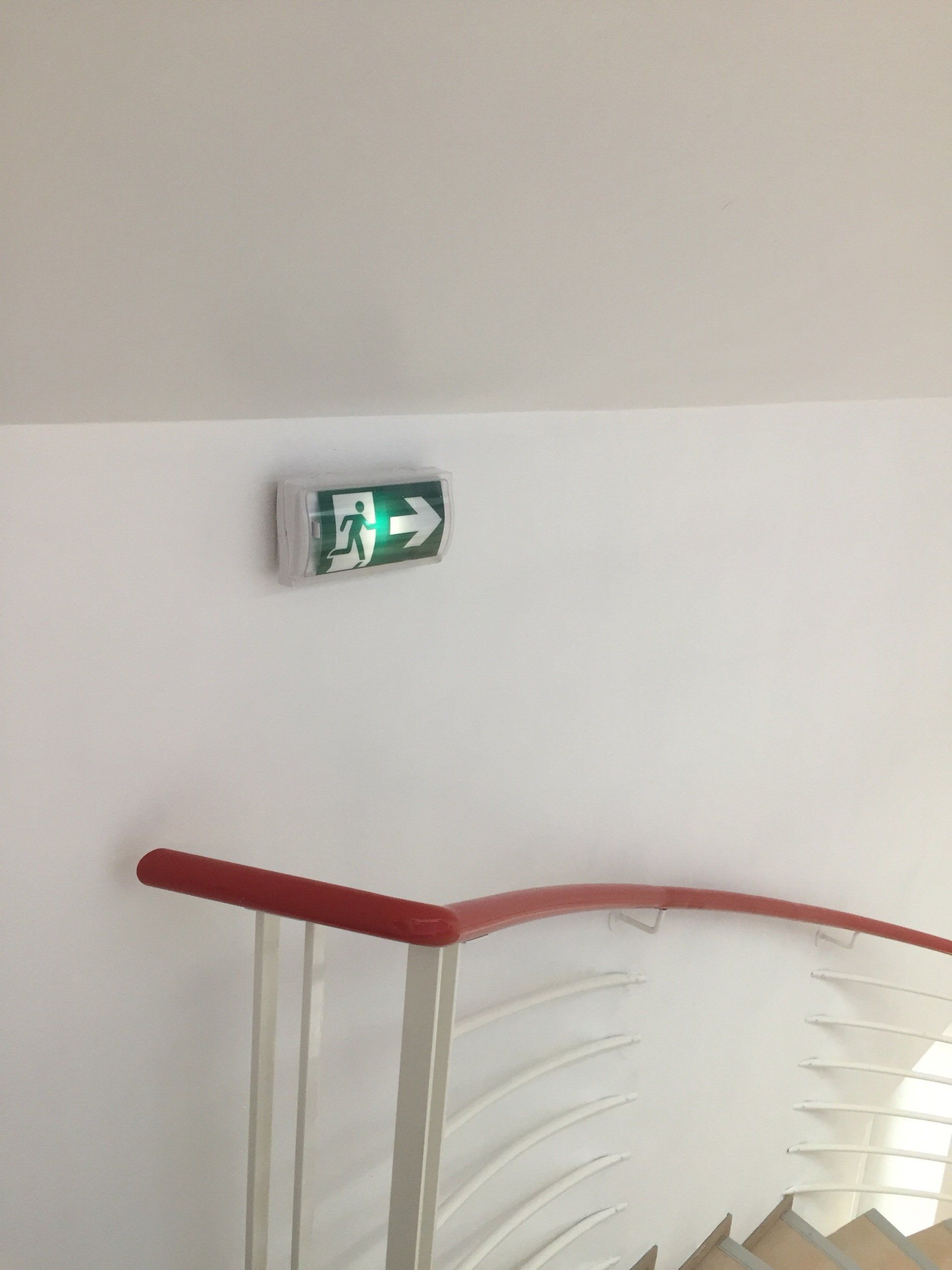 Un escalier avec une rampe rouge et un panneau de sortie vert sur le mur
