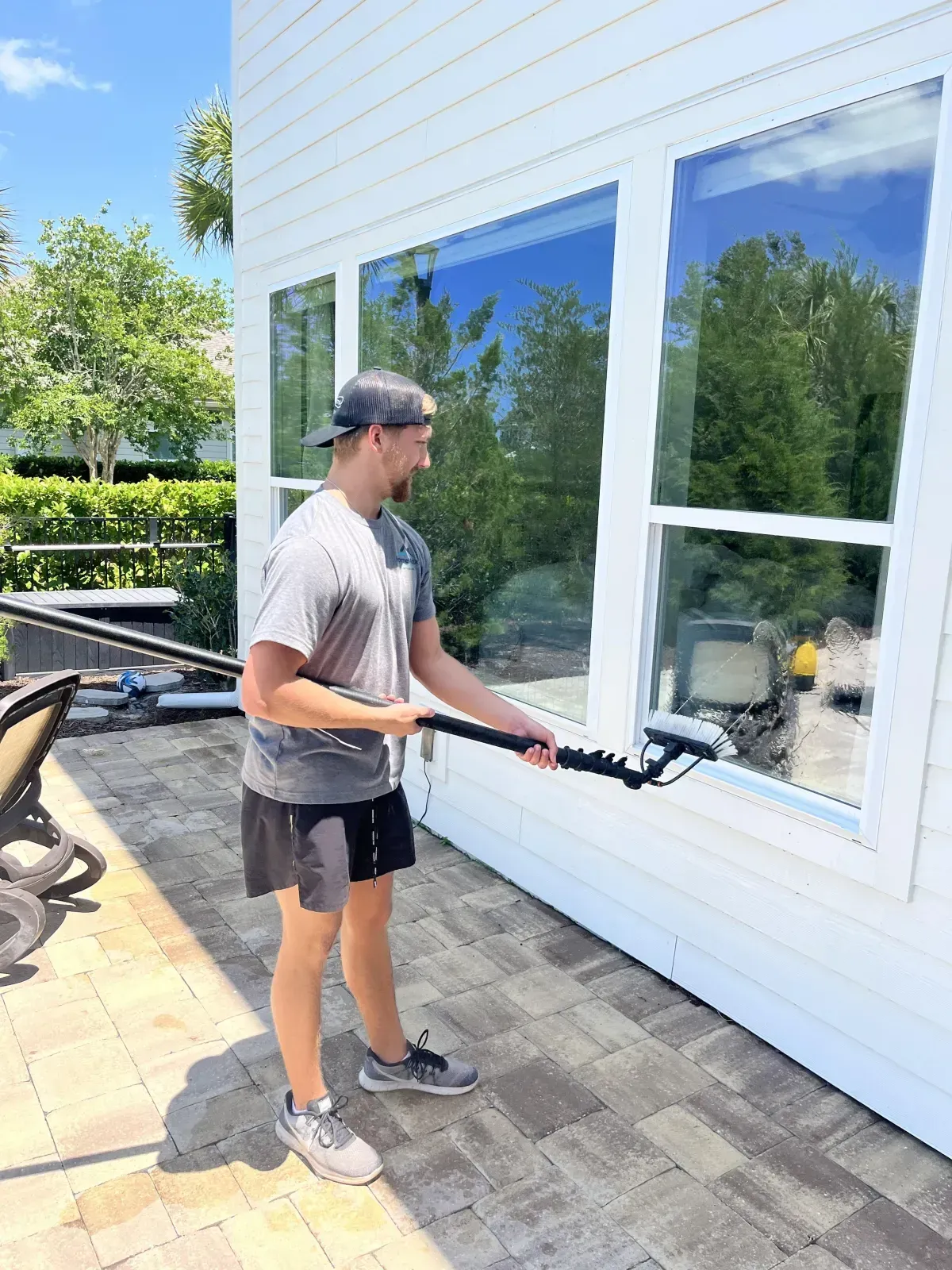 A man is cleaning a window with a hose on a patio.