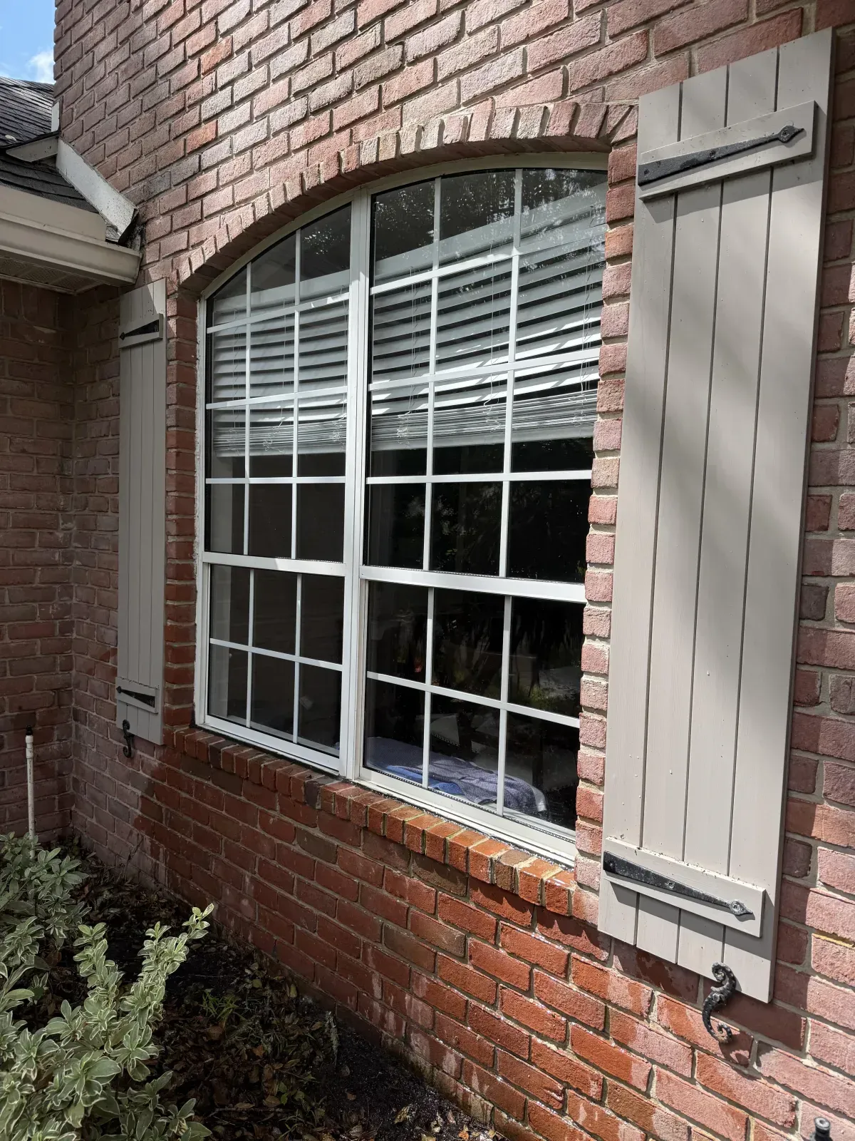 A large window on the side of a brick house with shutters.
