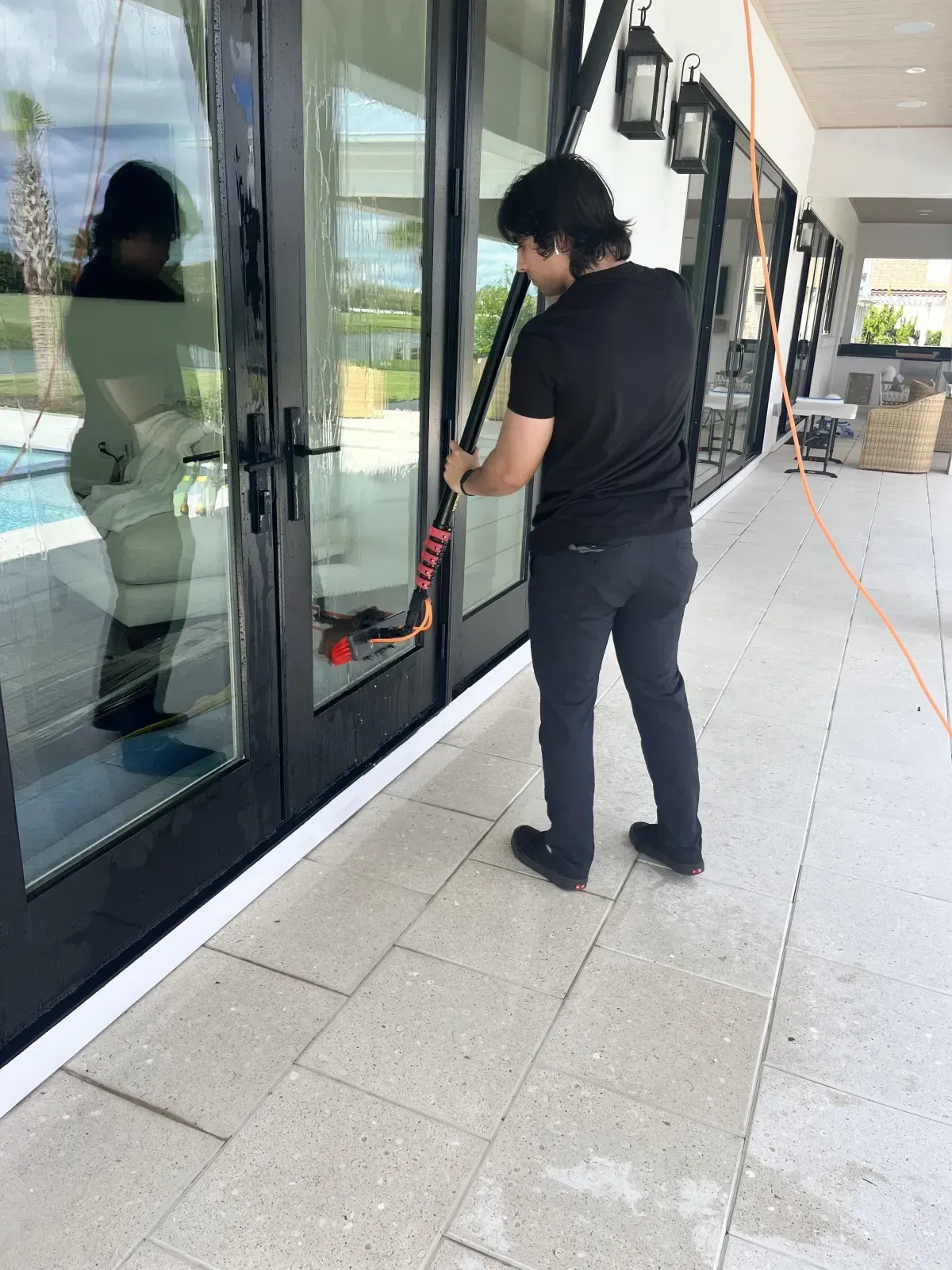 A man is cleaning a glass door with a vacuum cleaner.