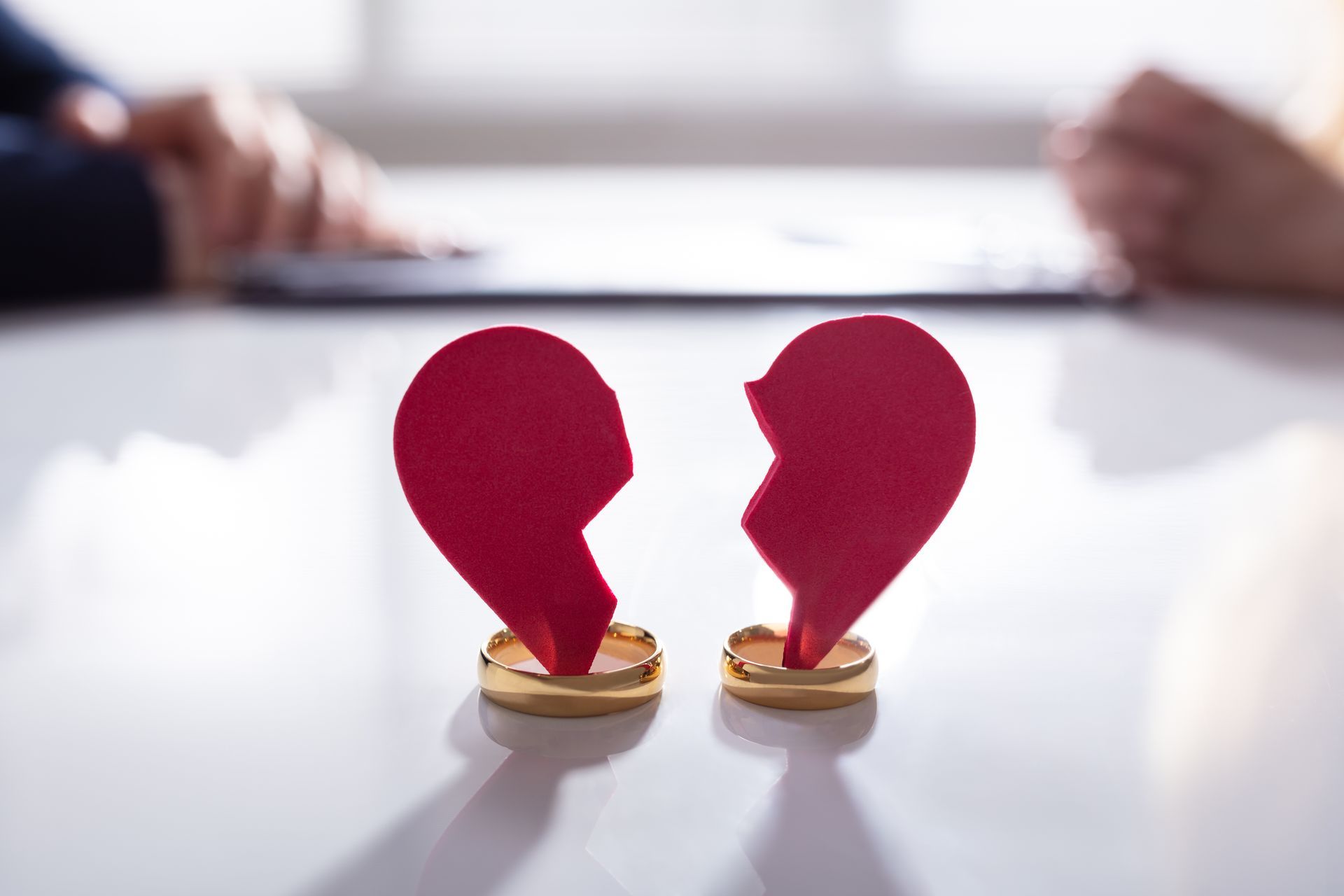 Broken heart halves on wedding rings, with two people's hands blurred in the background.