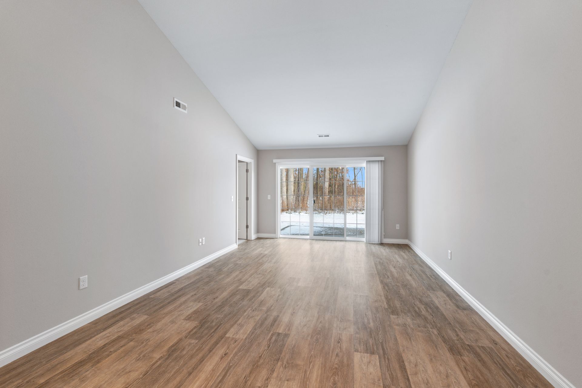 Empty room with wood flooring, light gray walls, and a sliding glass door.