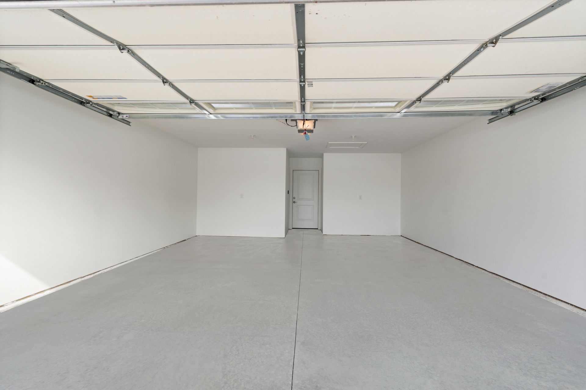 Empty, freshly painted white garage with gray epoxy floor, light fixture, and overhead garage door tracks.