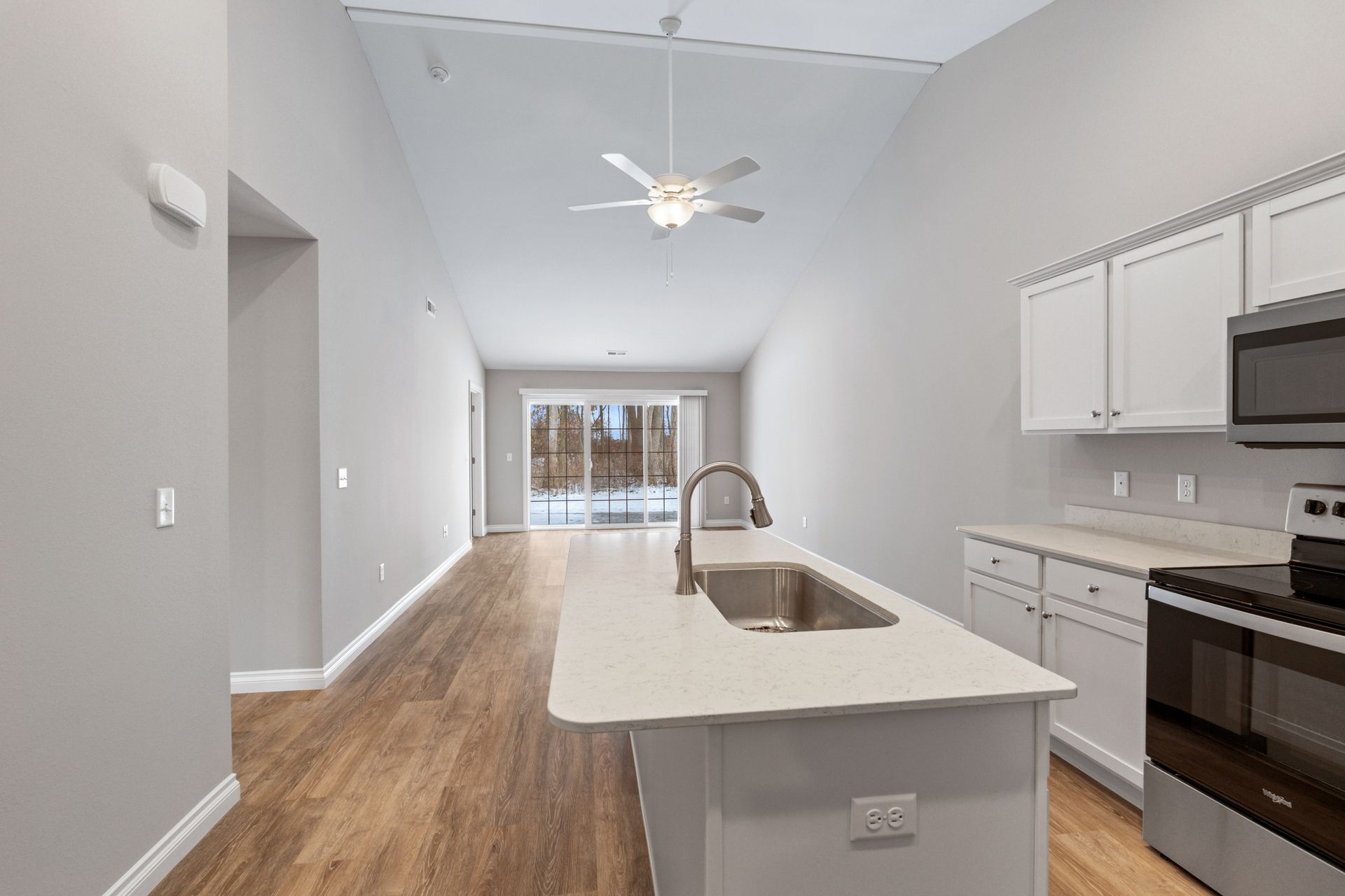 Kitchen and living space with light wood floors, white cabinets, and island with a sink.