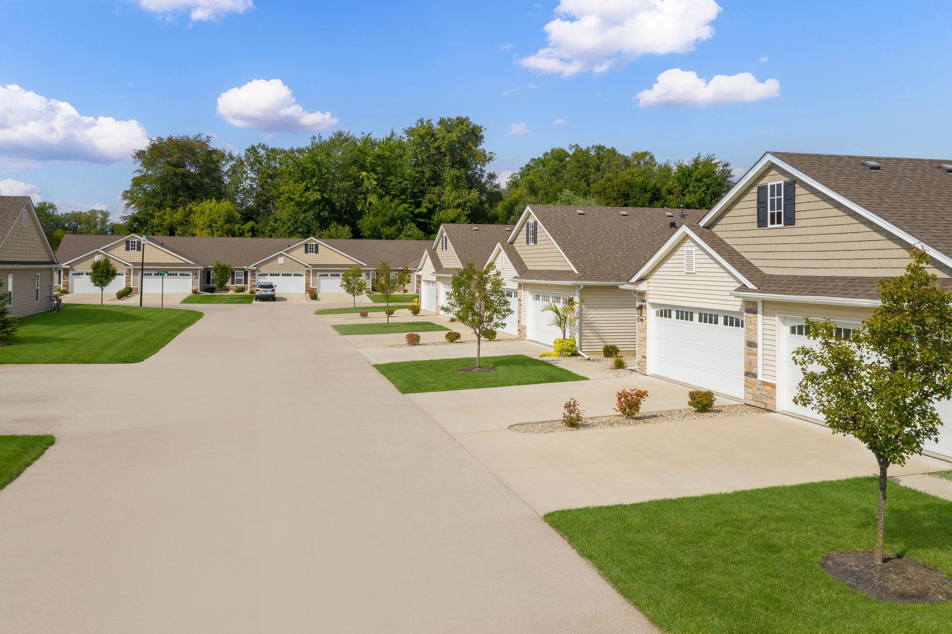 Row of beige houses with white garages, green lawns, and a concrete driveway under a blue sky.
