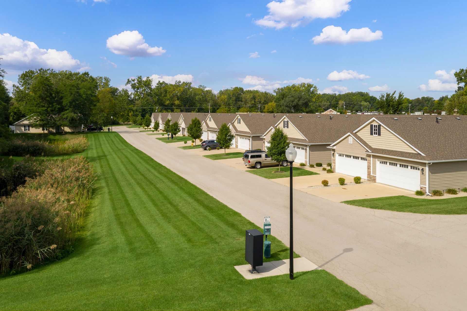 Row of beige townhouses with attached garages on a sunny day with green lawns and a blue sky.