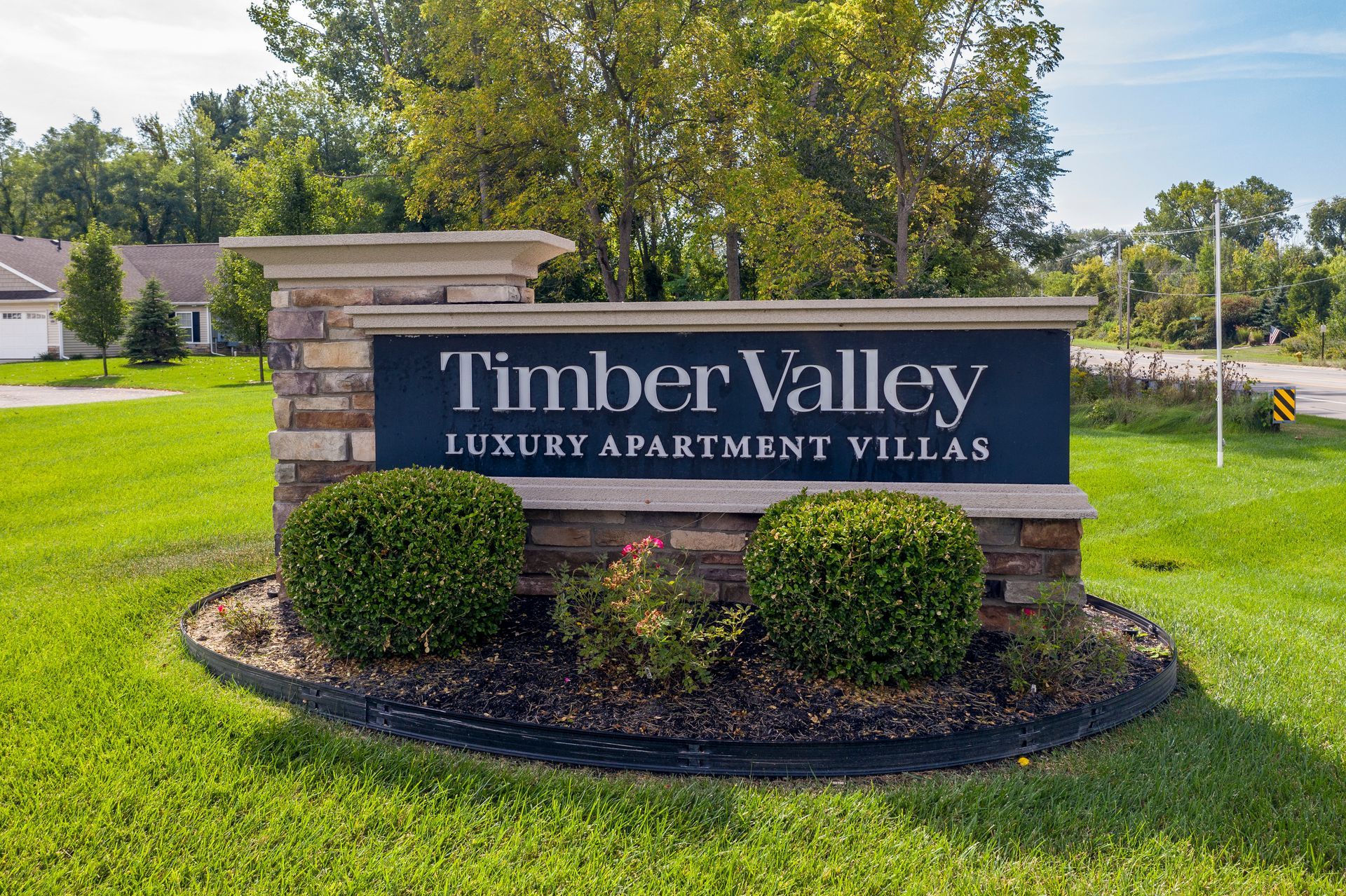 Sign for Timber Valley Luxury Apartment Villas, set in a grassy area with trees and blue text.