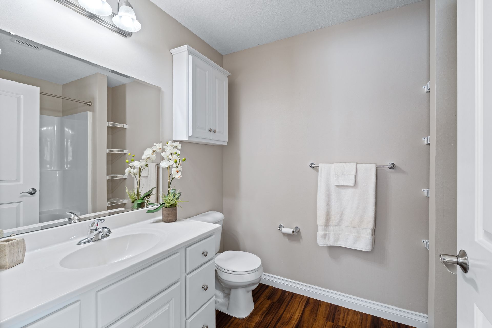 Bathroom with white vanity, toilet, and cabinet; tan walls, brown floor.