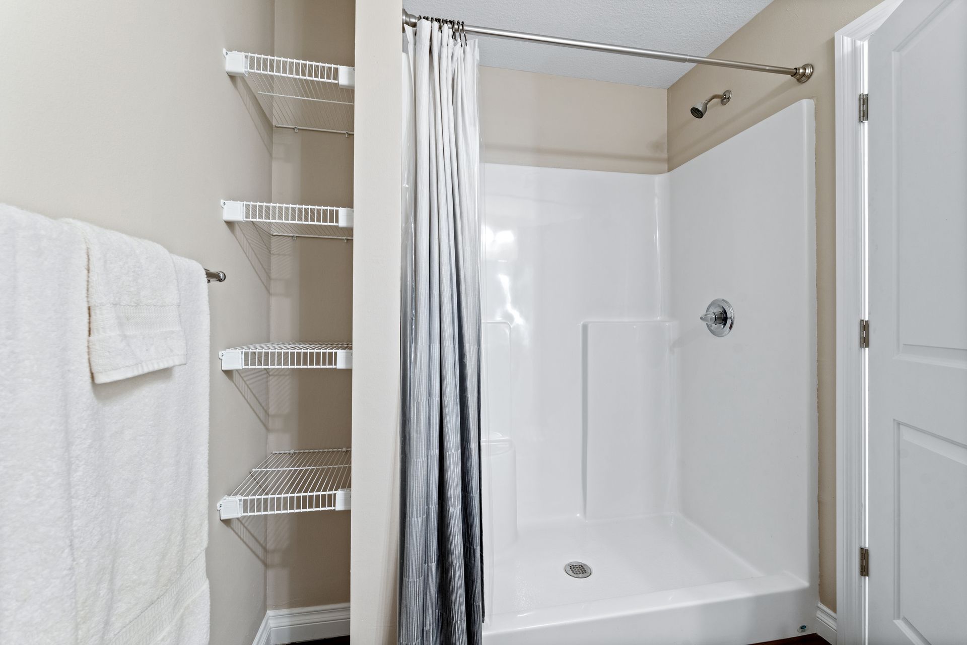 White shower stall with a gray curtain, shelving, and a towel rack.
