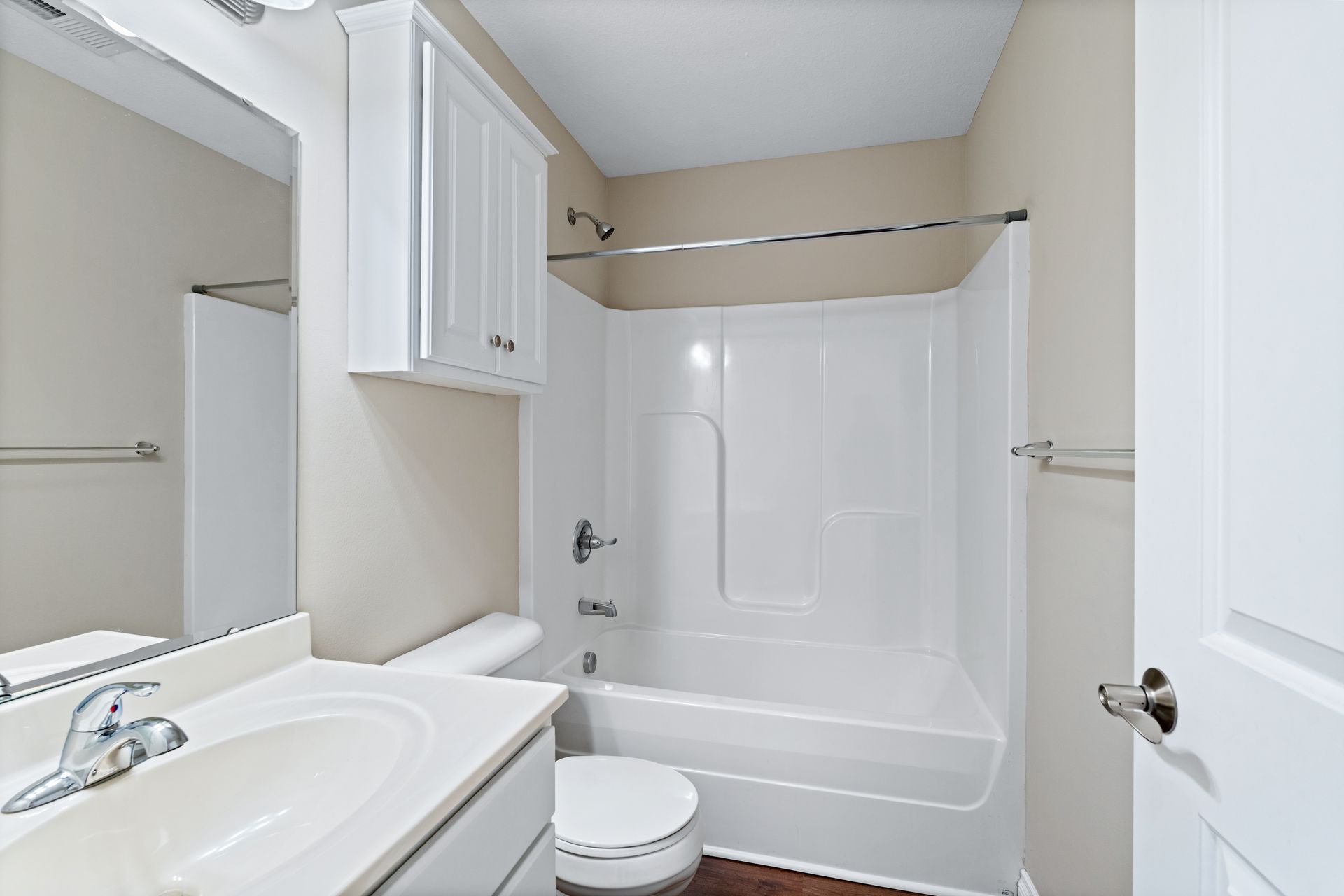 Bathroom with white tub, toilet, and vanity, beige walls, and a closed cabinet.