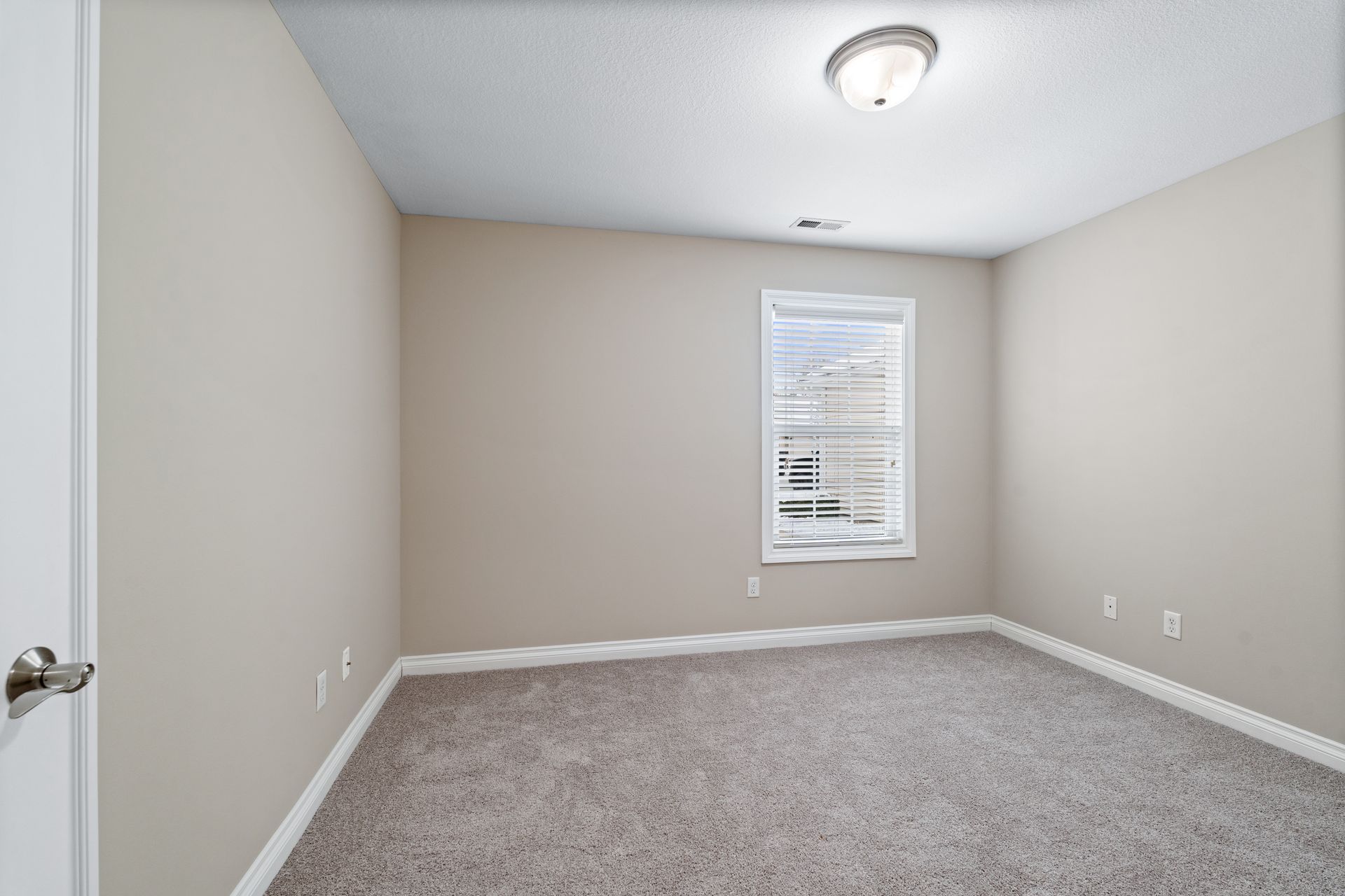 Empty room with beige walls, carpet, window, and ceiling light.