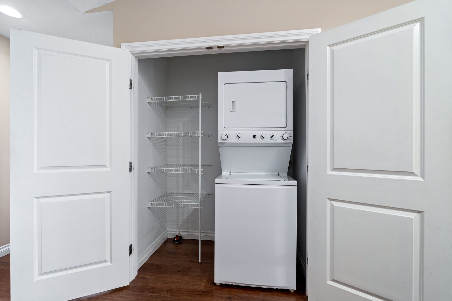 Closet with stacked white washer and dryer, open white bi-fold doors, and wire shelving.