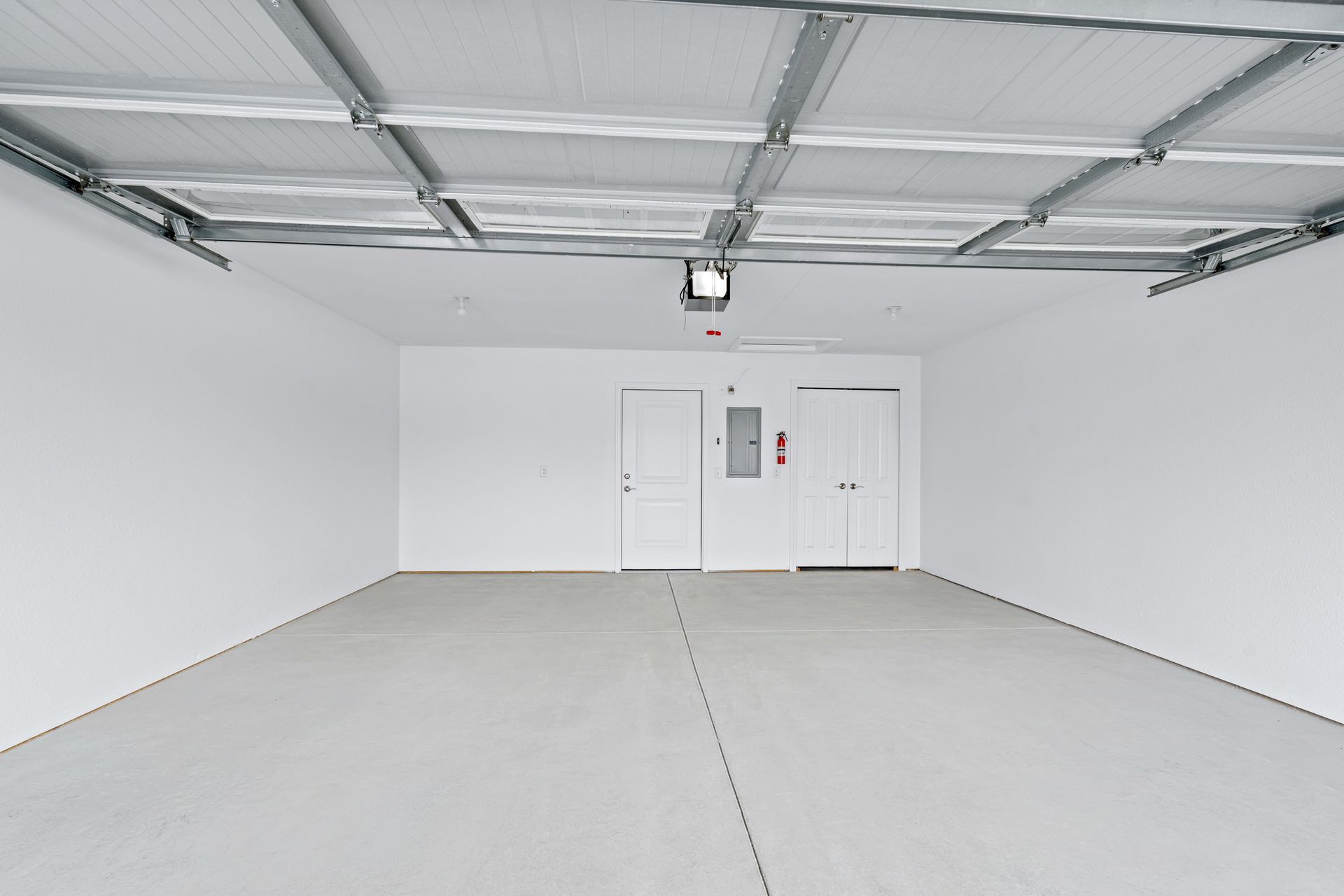 Empty, white-walled garage with gray floor and ceiling. Two doors and electrical panel are visible at the back.