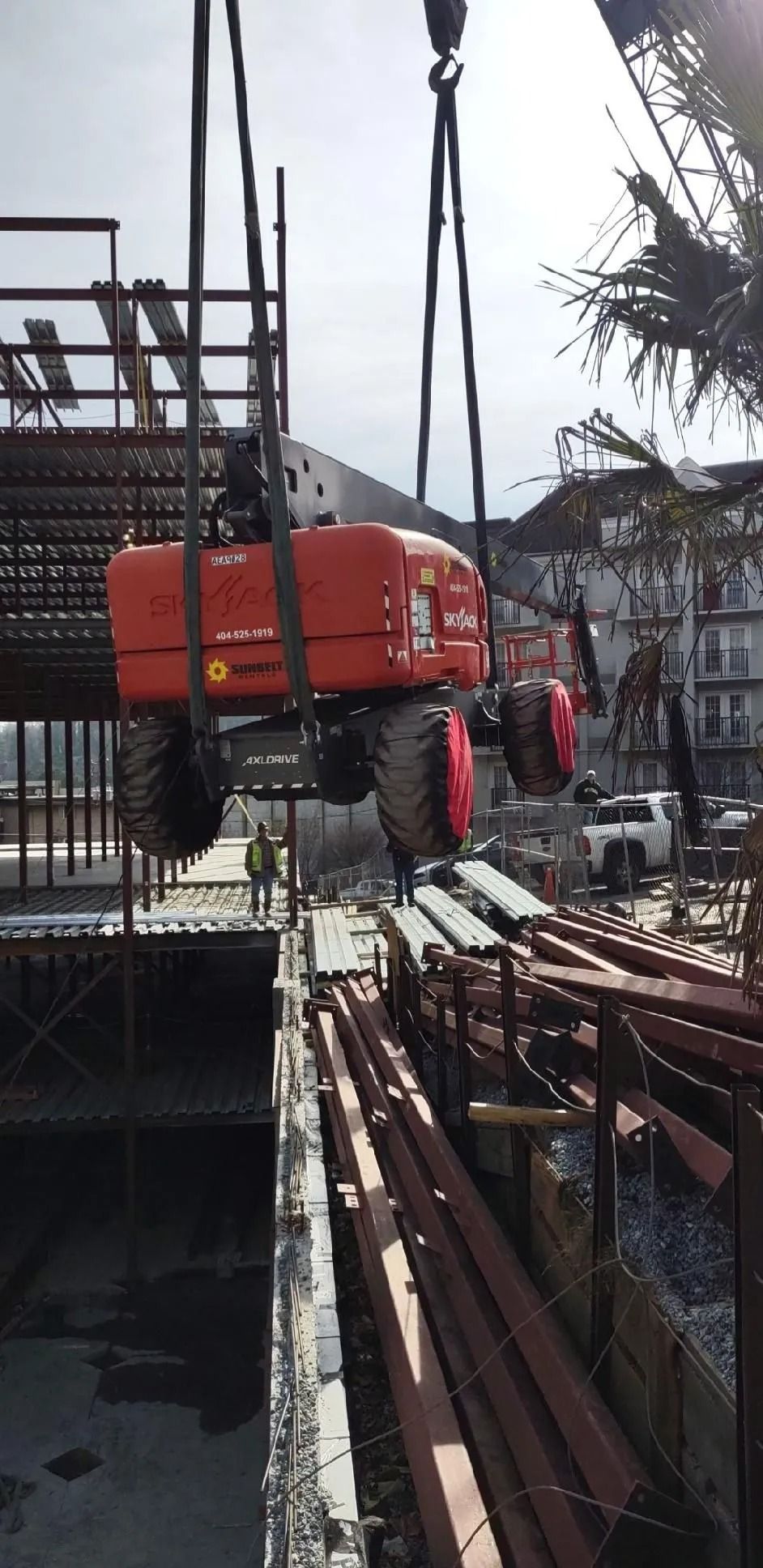 A crane lifting an orange construction lift at a construction site.