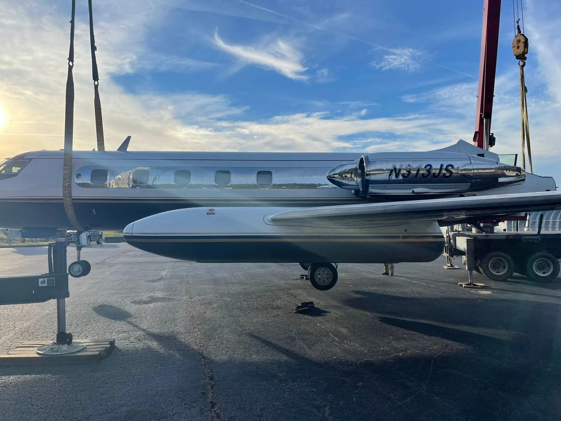 A business jet being lifted by a crane onto a trailer, with bright sky in the background.
