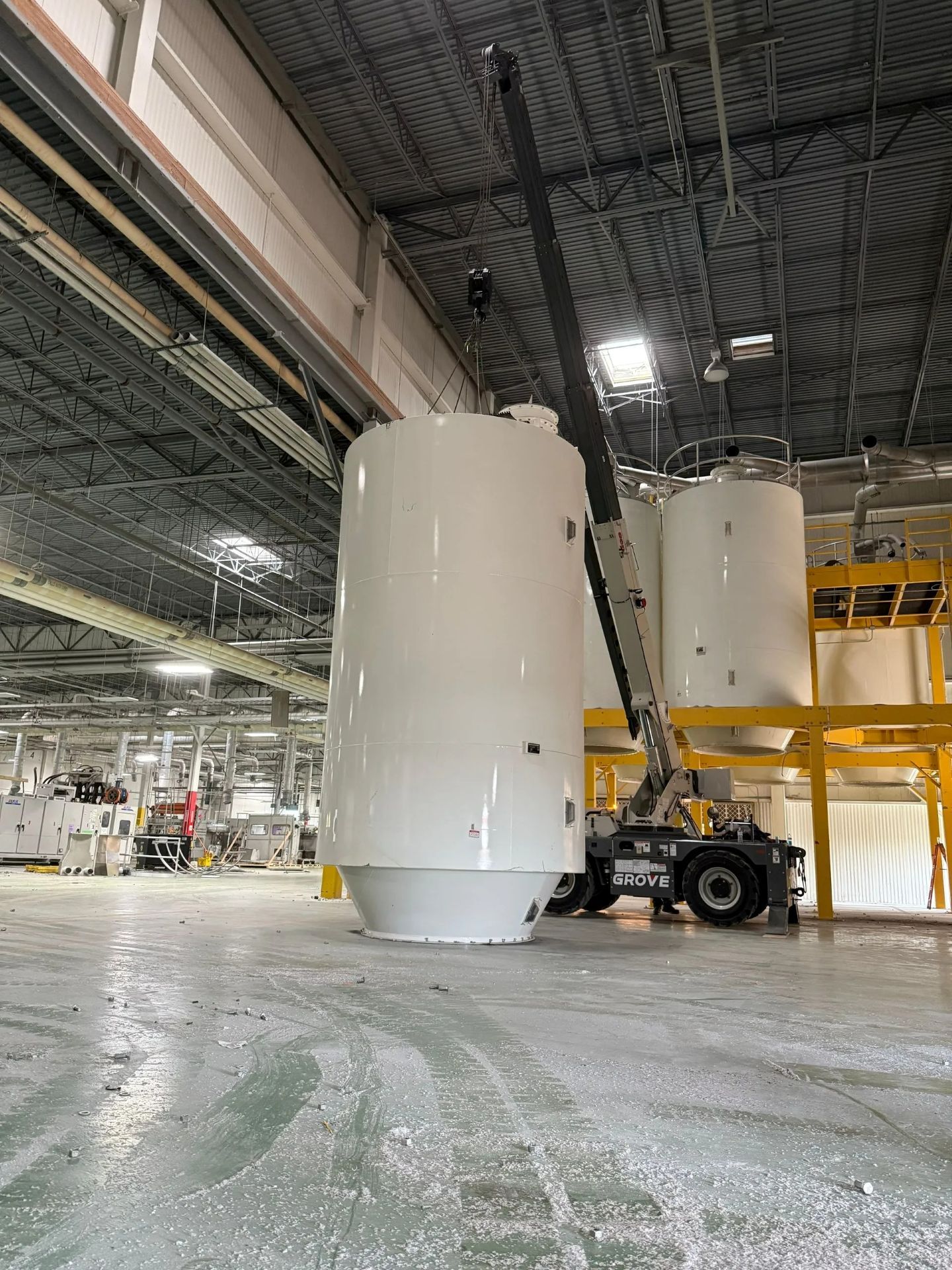 White industrial tank being lifted by a crane in a factory setting.
