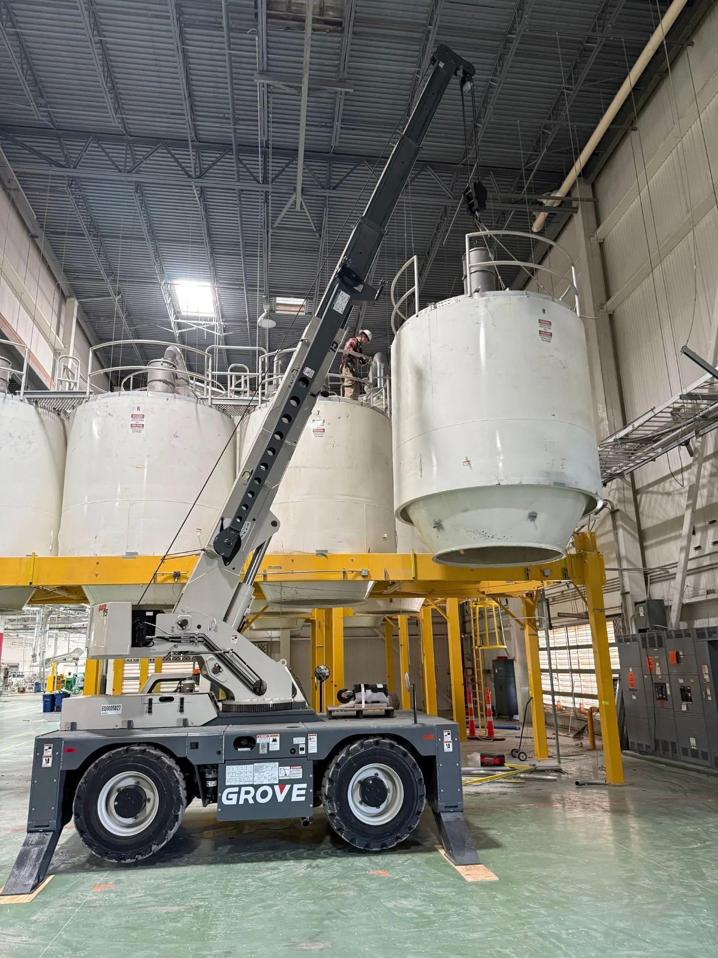 A Grove crane lifting a large white cylindrical tank inside a factory.