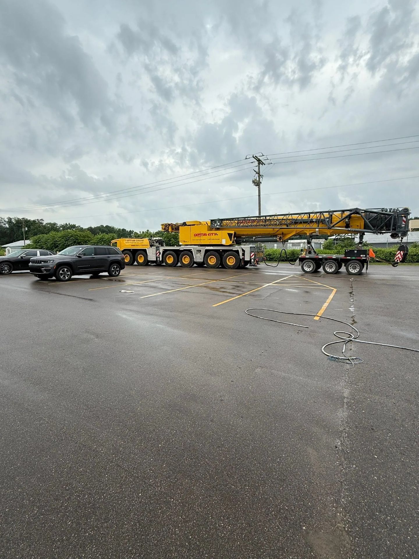 Large yellow crane on a multi-axle trailer in a parking lot, gray sky overhead.