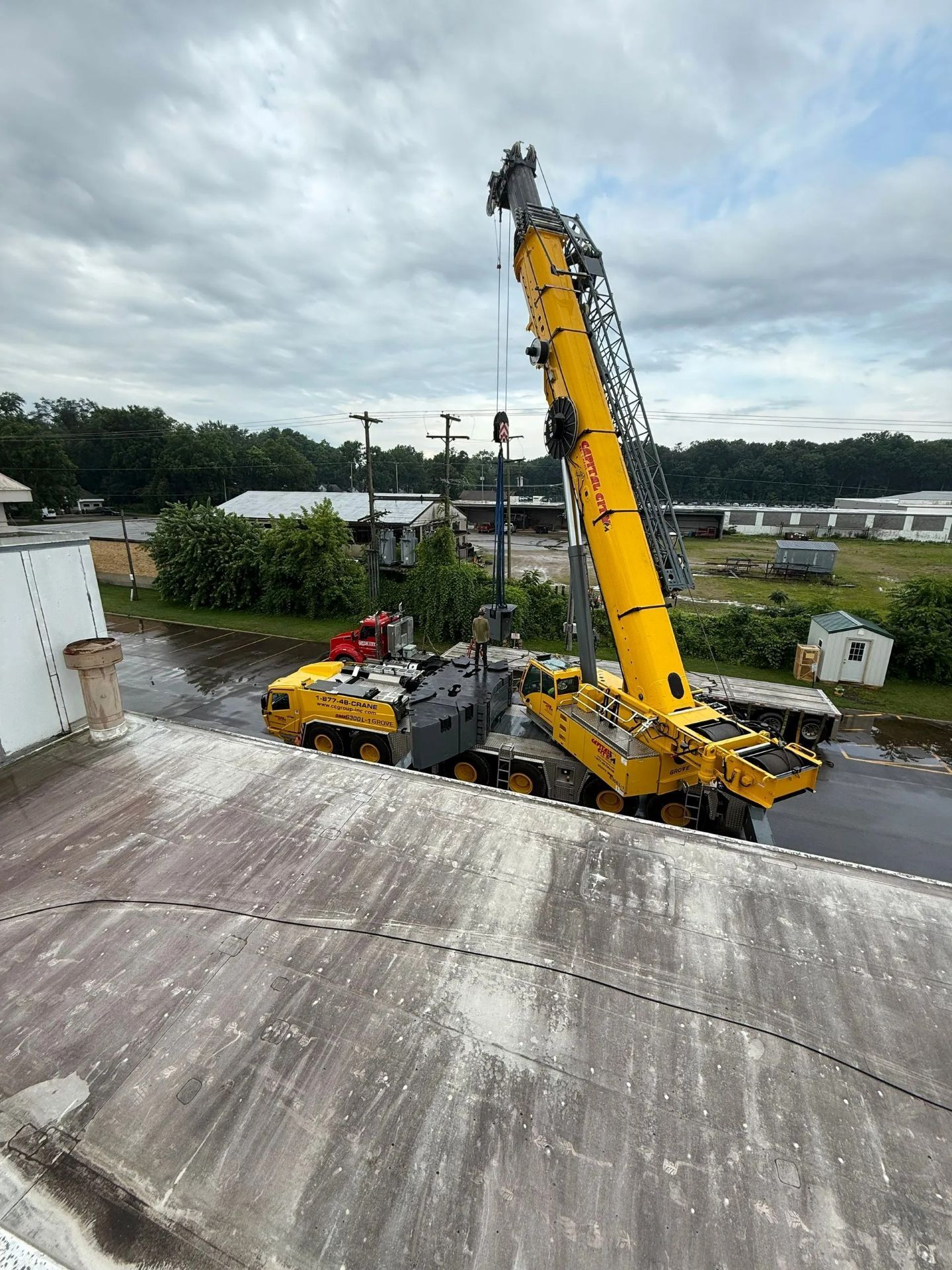 Yellow crane lifting a utility pole near a building, against an overcast sky.