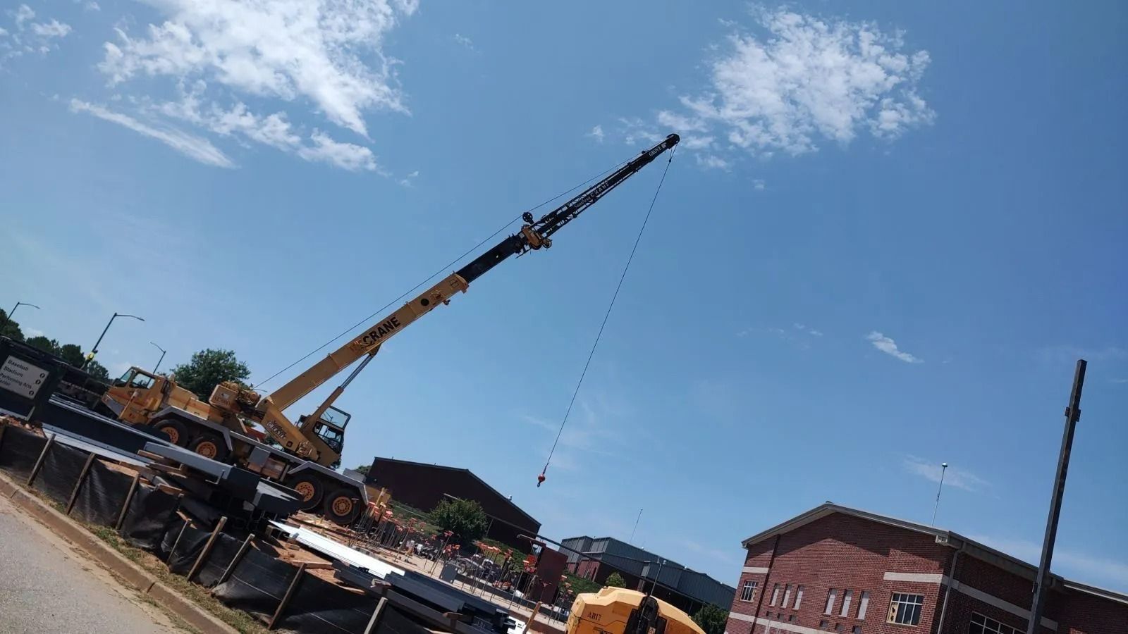 A large yellow crane lifting something at a construction site against a blue sky with some clouds.