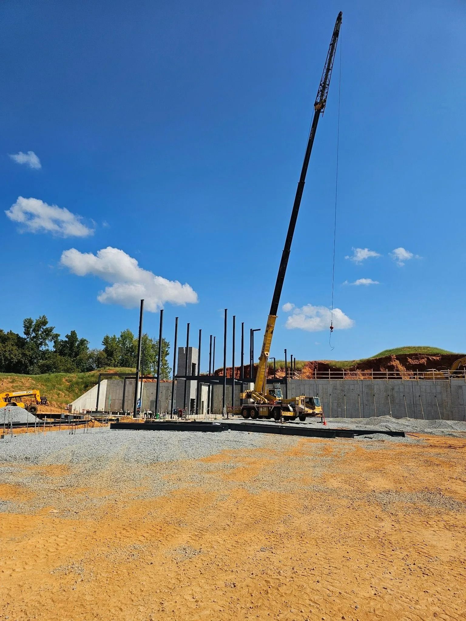 Construction site with a tall crane, concrete base, metal beams, and bright blue sky.