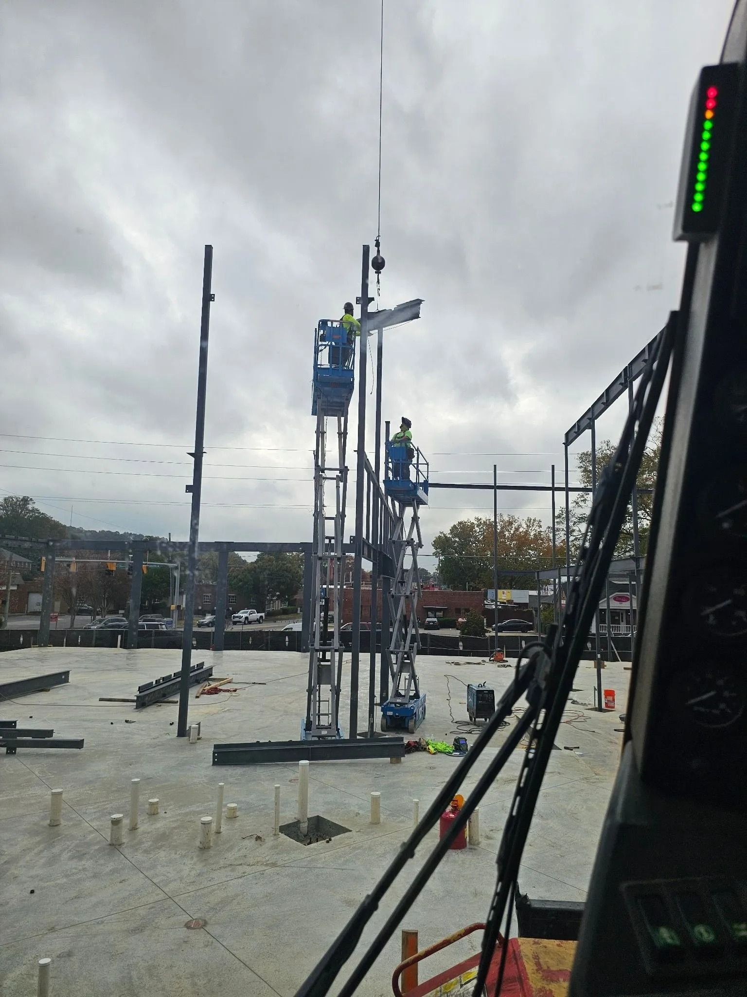 Construction workers on lifts assembling steel framing, cloudy outdoor setting.
