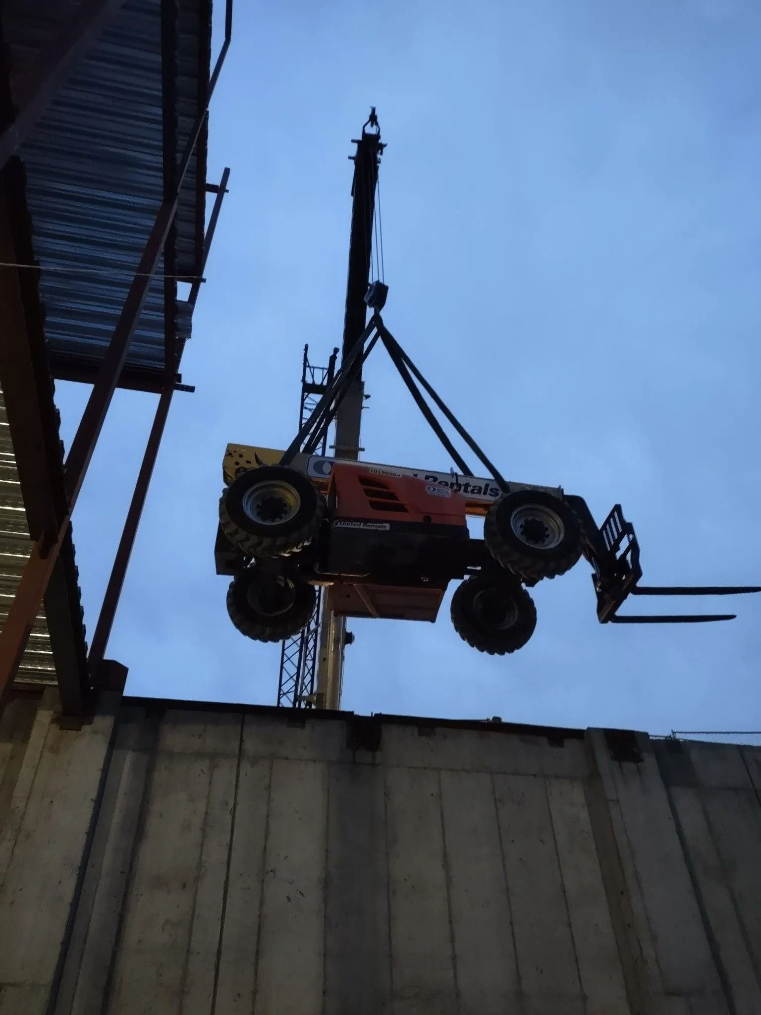Orange forklift suspended in the air over a concrete structure, blue sky in the background.
