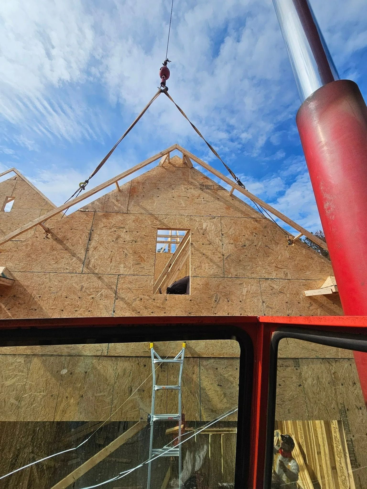 Construction crane lifting a roof truss onto a building under construction, against a cloudy sky.